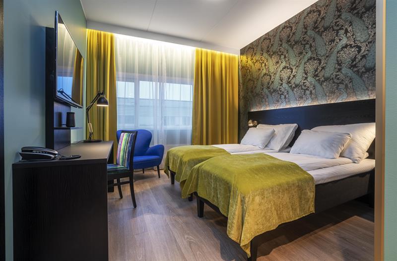 hotell rom med ddobbeltseng med gult sengeteppe og en blå stol