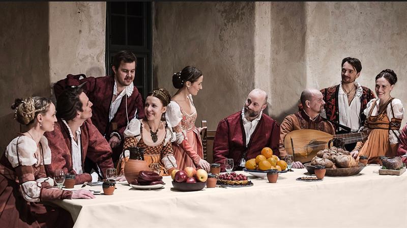 Skuespillere i oppsetningen Musica in Castello rundt et bord med fruktfat - kledd i historiske klær