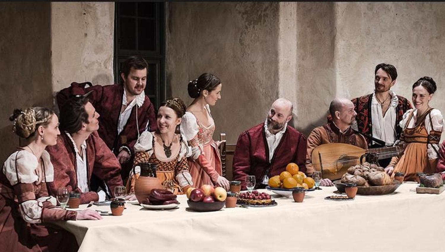 Skuespillere i oppsetningen Musica in Castello rundt et bord med fruktfat - kledd i historiske klær