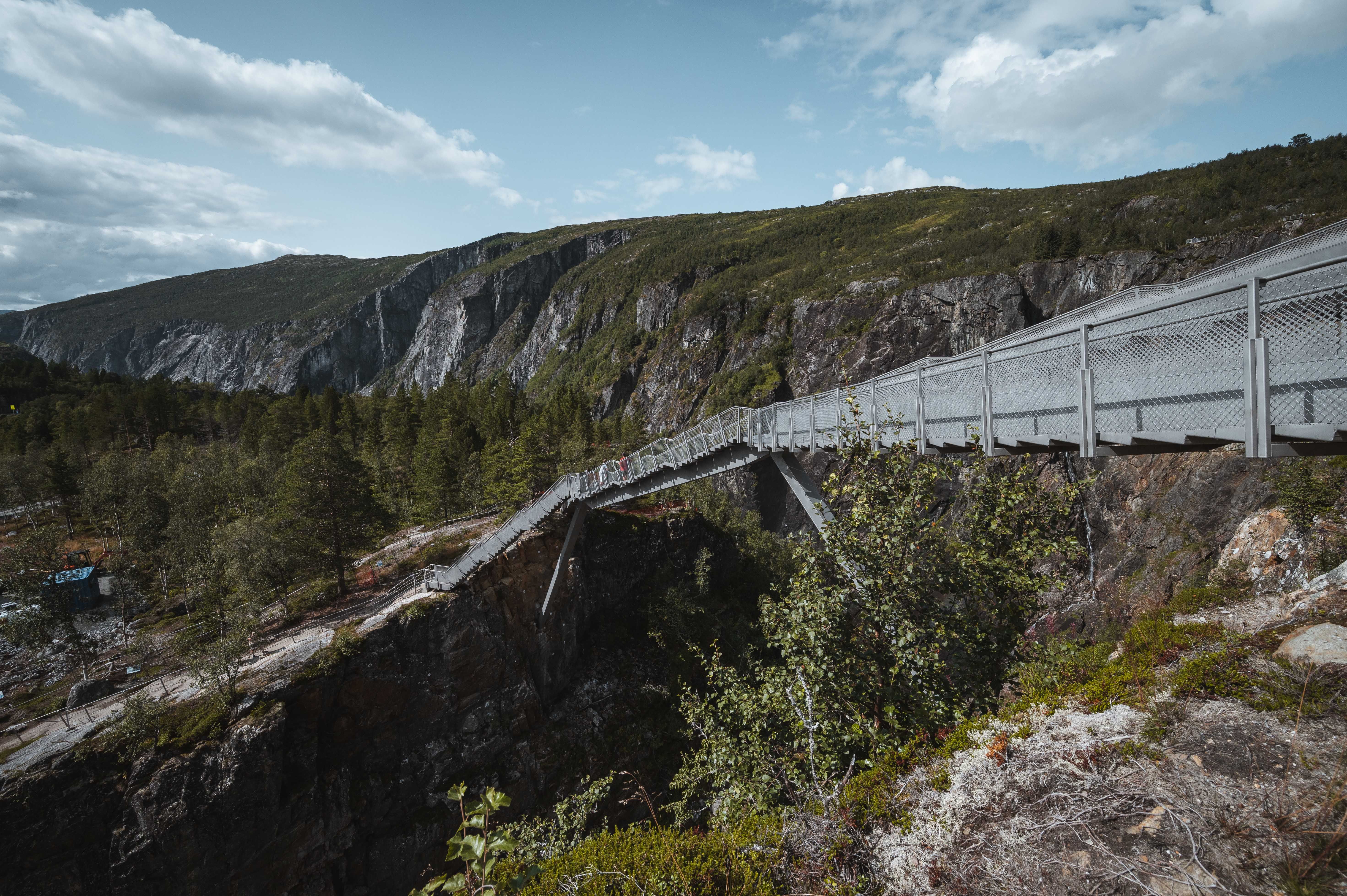 Gangbru strekkjer seg over juvet ved Vøringsfossen, omgitt av fjell og tre.