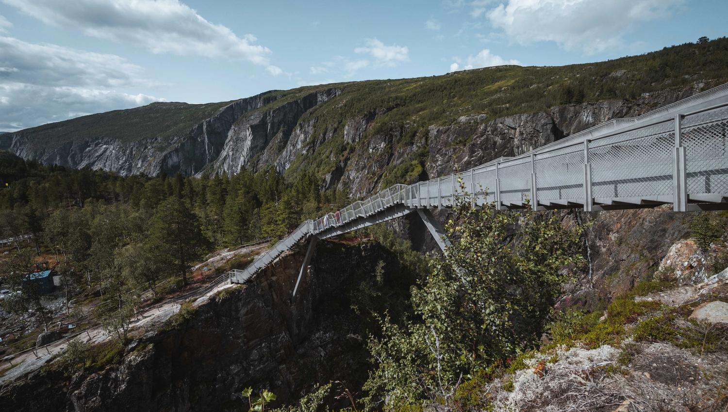 Gangbru strekkjer seg over juvet ved Vøringsfossen, omgitt av fjell og tre.