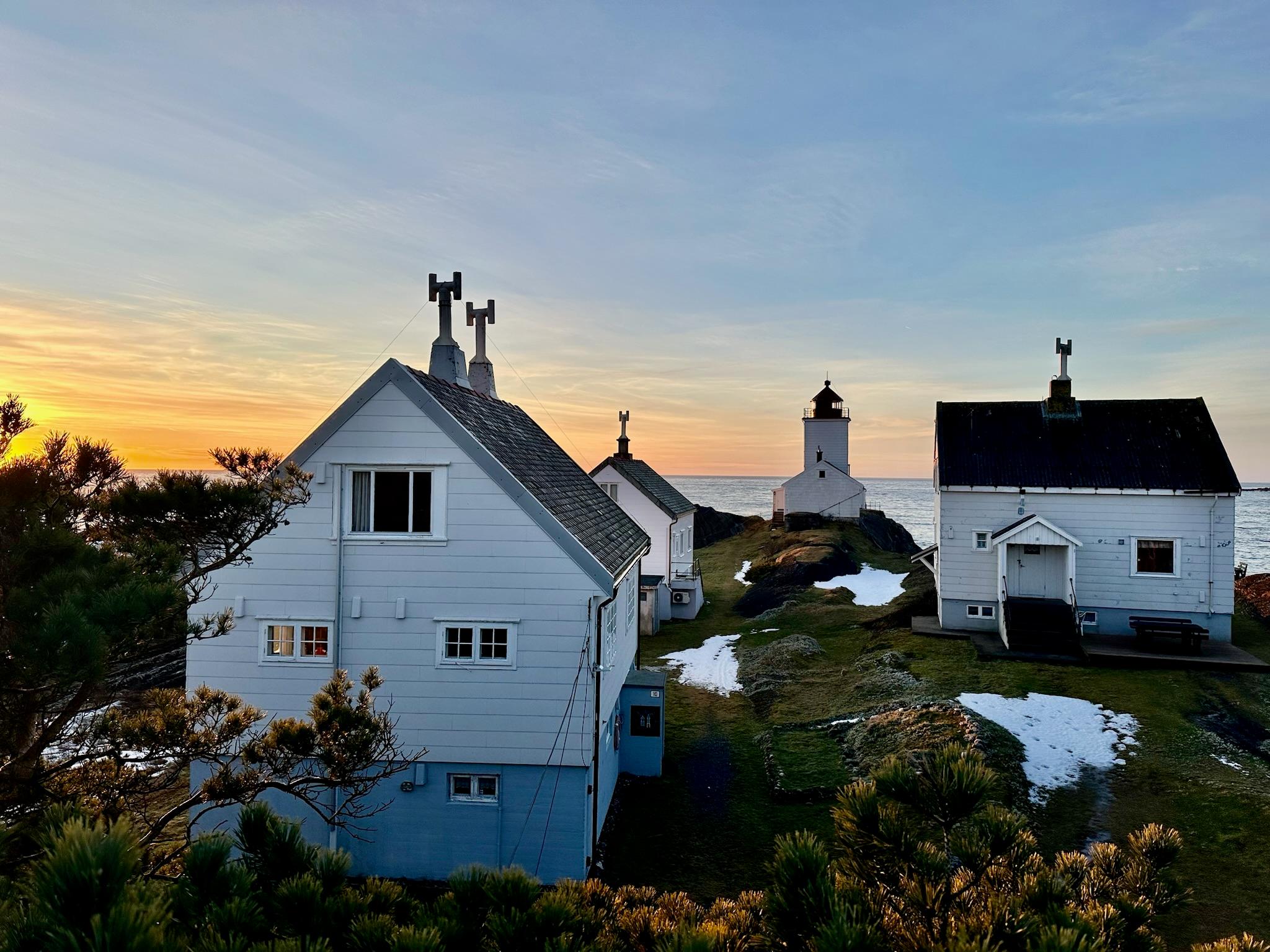 hvite hus med fyrhus i bakgrunn, gul oransje himmel