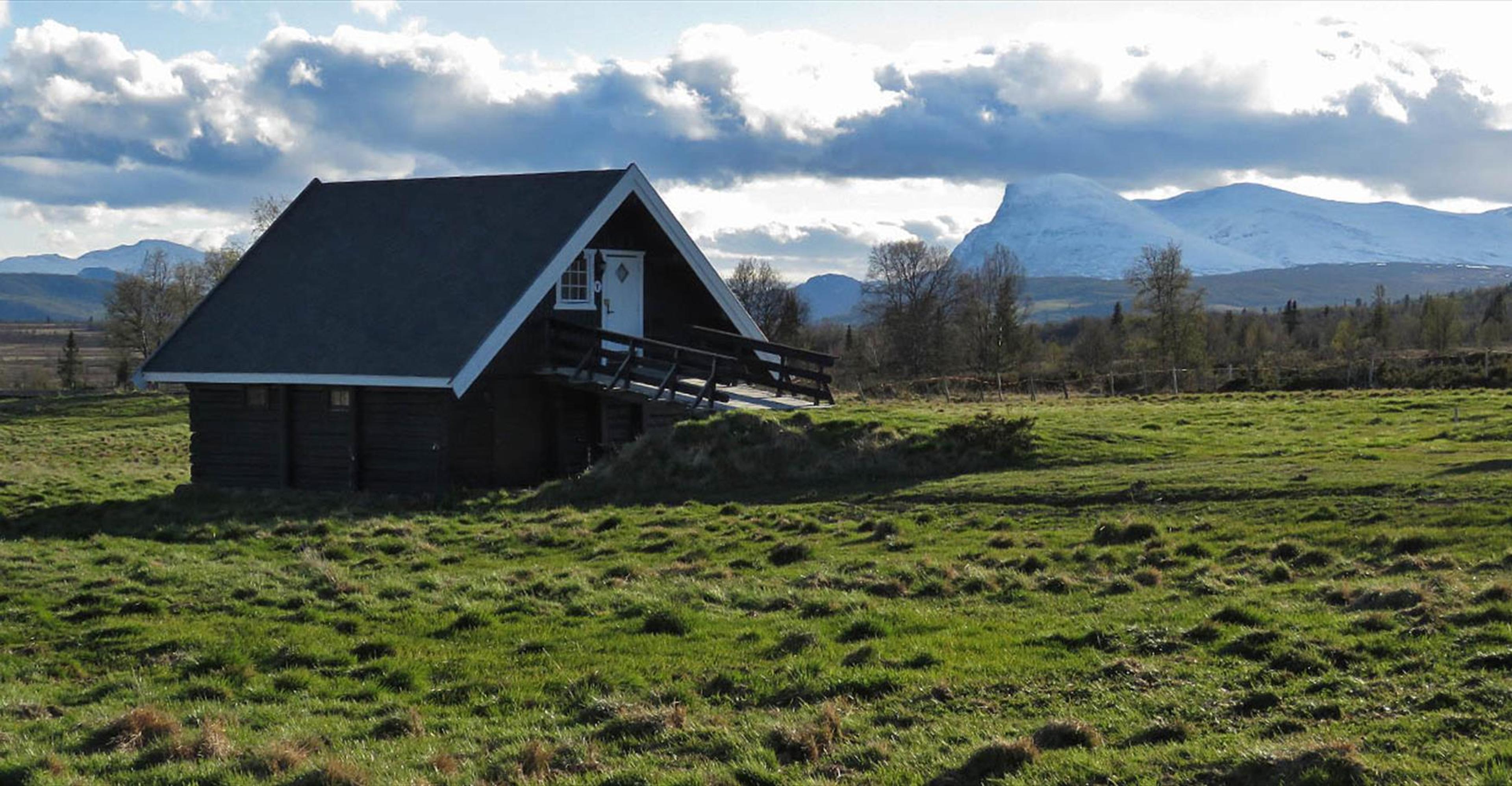 Tyrishølt en delvis skyet sommerdag, med grønt gress utenfor og snøkledde fjell i horisonten.