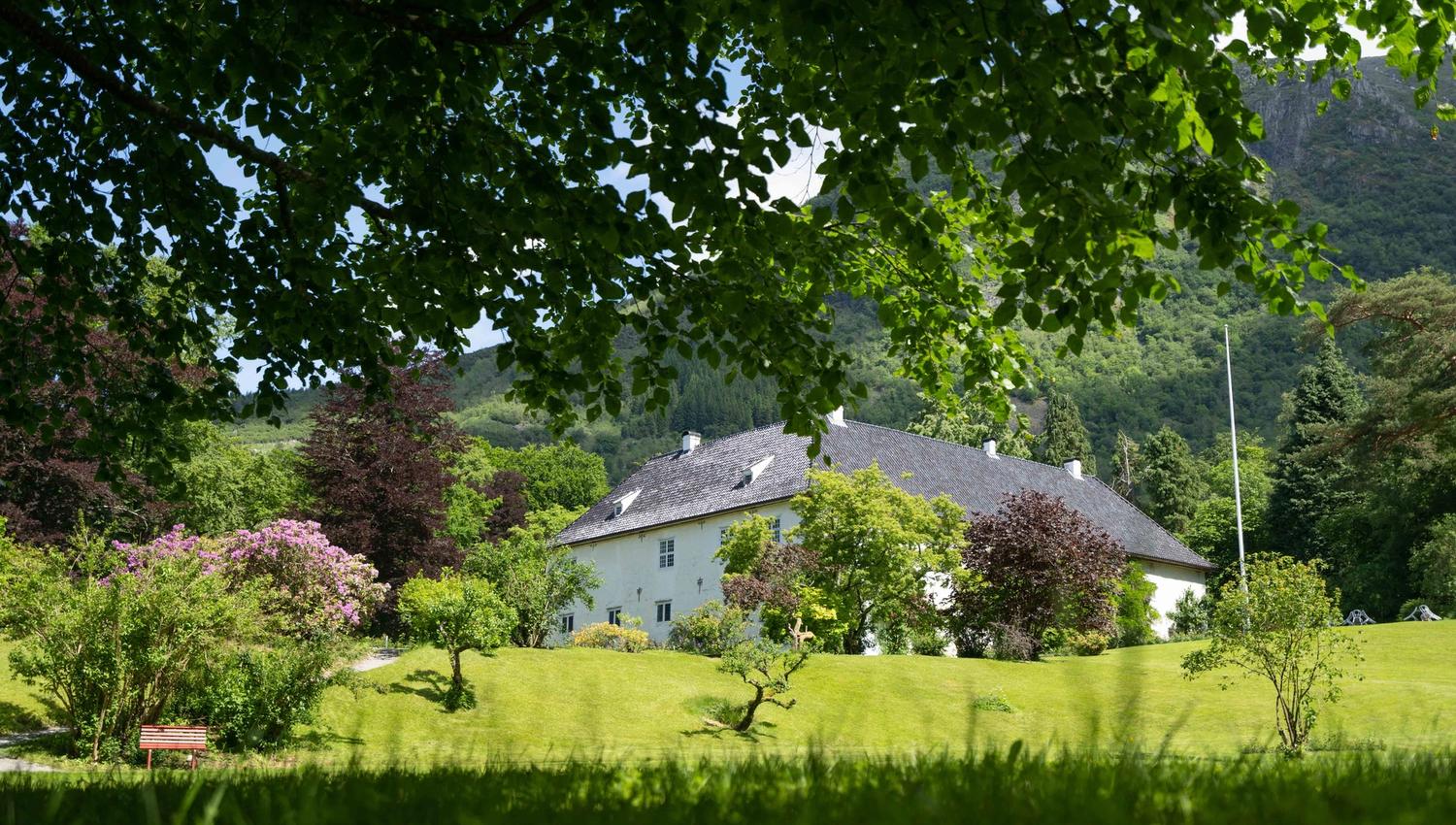 Baroniet Rosendal sett frå parken, omgitt av grøne tre og fjell.