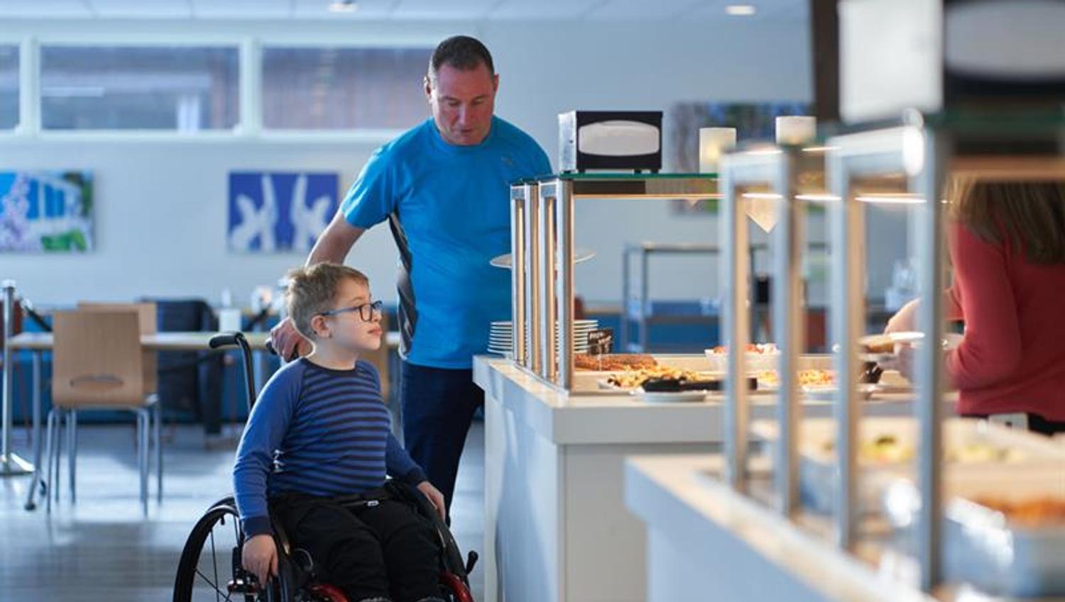 boy in a wheelchair with his father at the breakfast buffet in Hotell fritidsparken