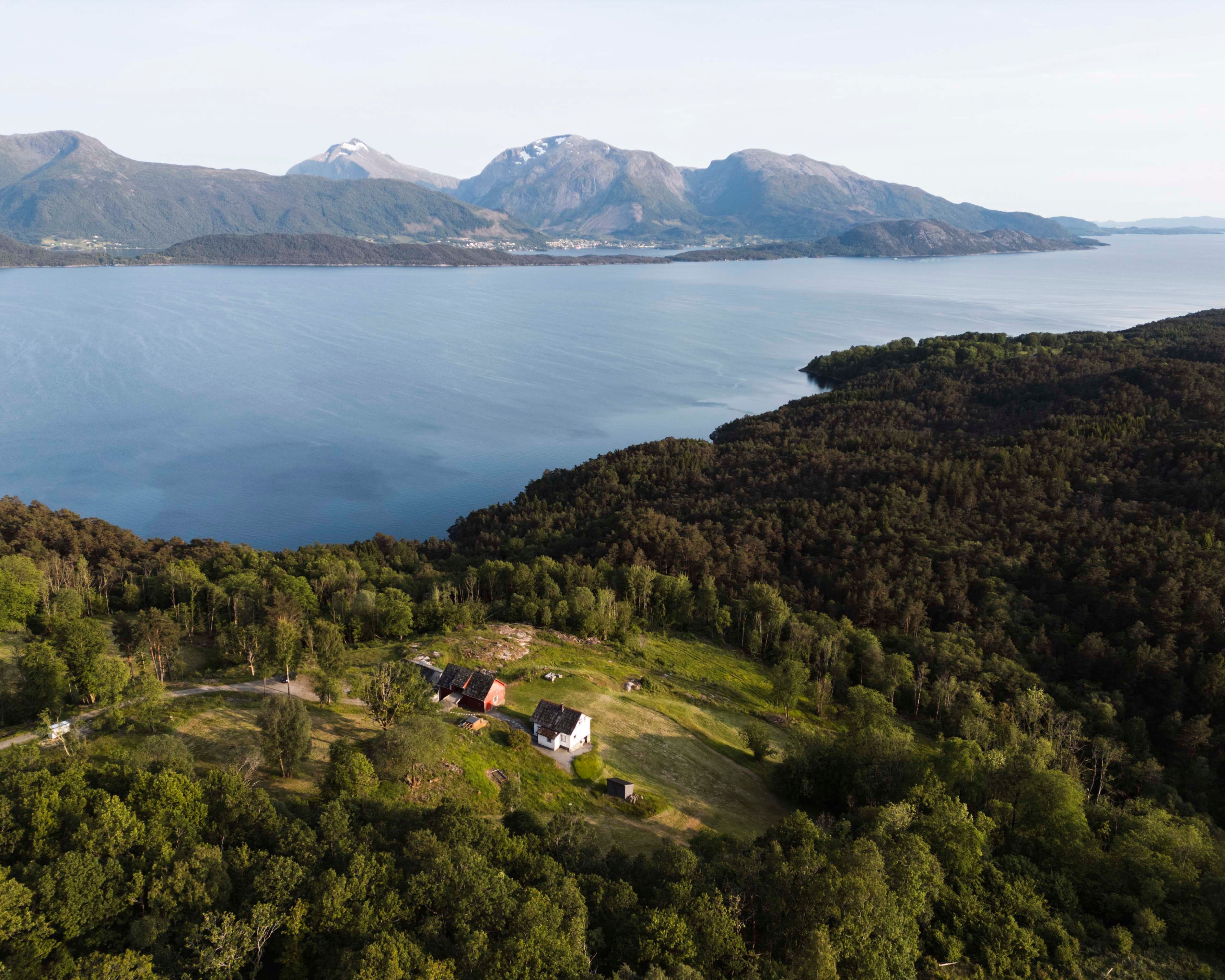 Dronebilde av Stigen Fjordlodge omgitt av fjord, fjell og skog i Hardanger.