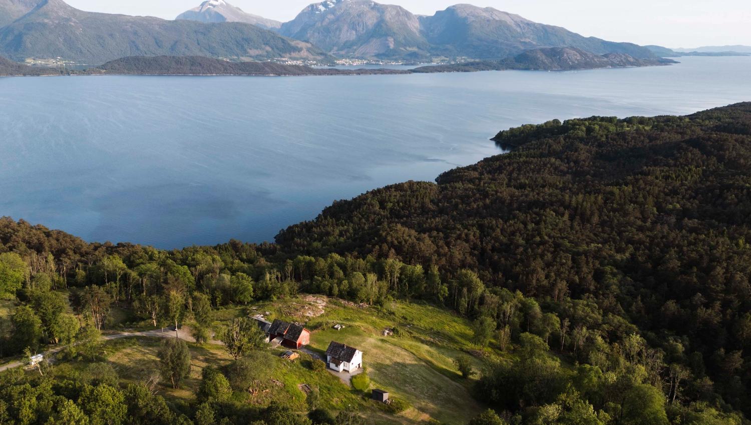Dronebilde av Stigen Fjordlodge omgitt av fjord, fjell og skog i Hardanger.