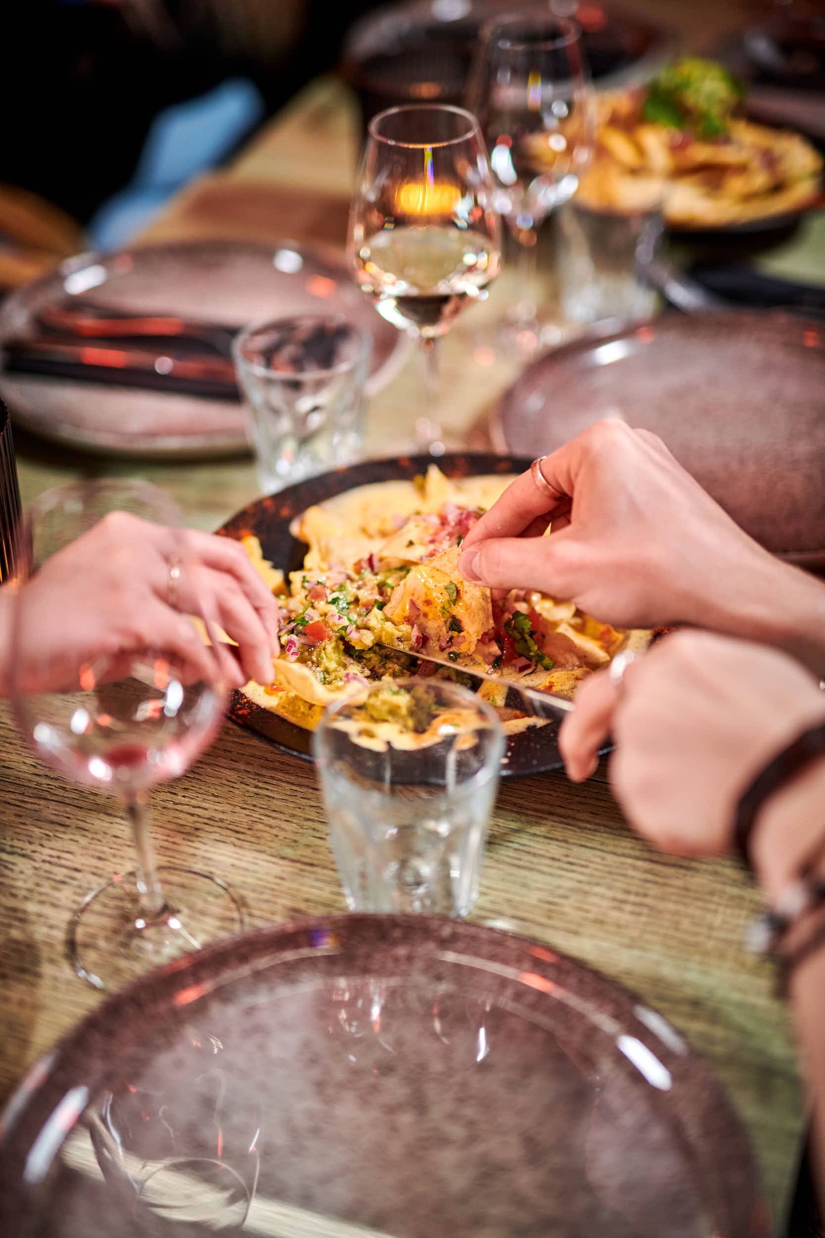 Personer deler en tallerken nachos ved et bord med vin og vann.