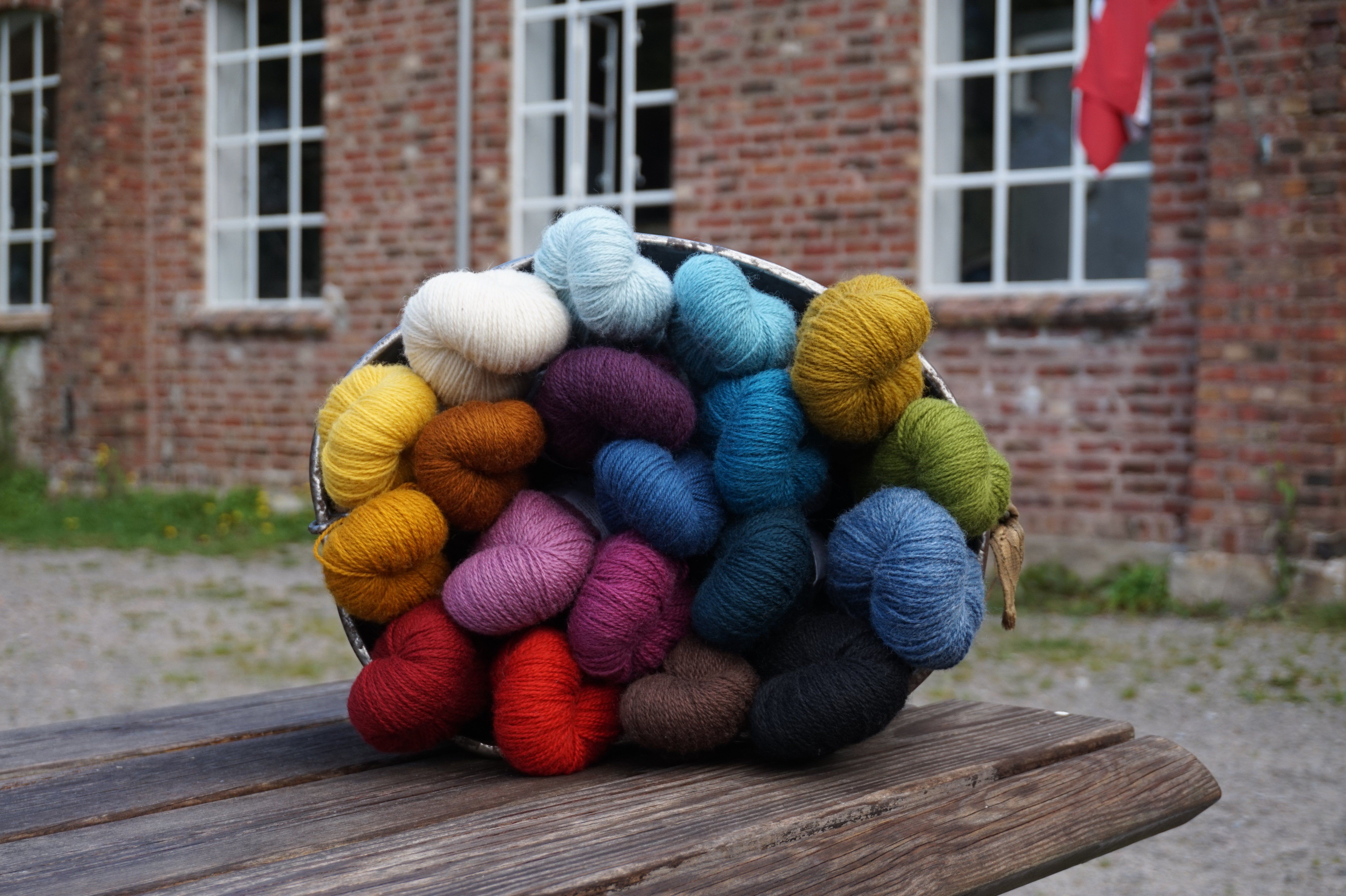 Bucket of yarn in various colors: red, burgundy, brown, dark blue, blue, light blue, yellow, orange, mustard yellow, white, purple, pink.