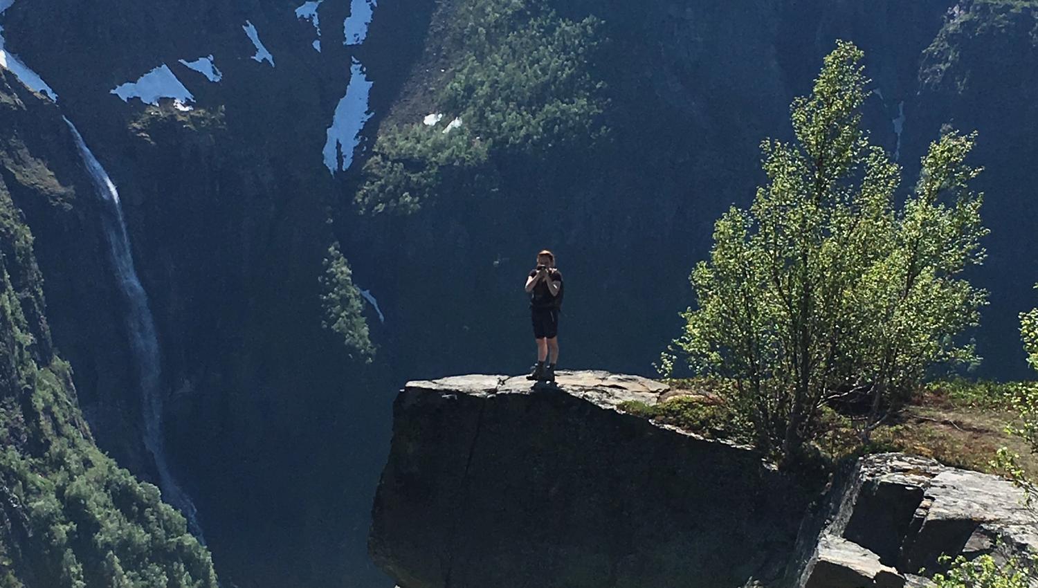 Person standing on a mountain ledge overlooking steep cliffs and a waterfall in Hardanger.