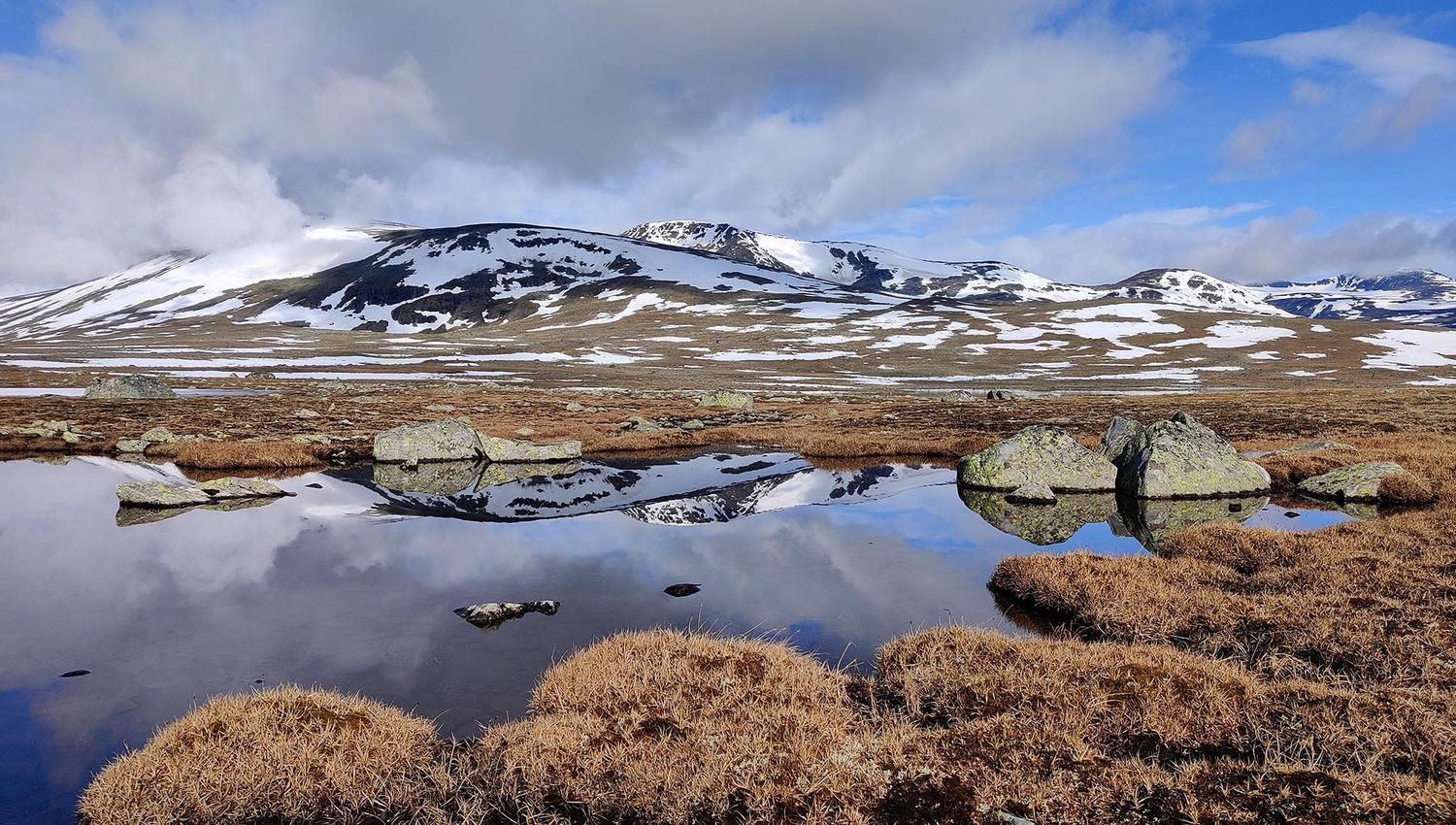 snødekte fjell speiler seg i blikkstille fjellvann