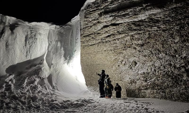A group of people standing with headlamps, lighting up the frozen waterfall