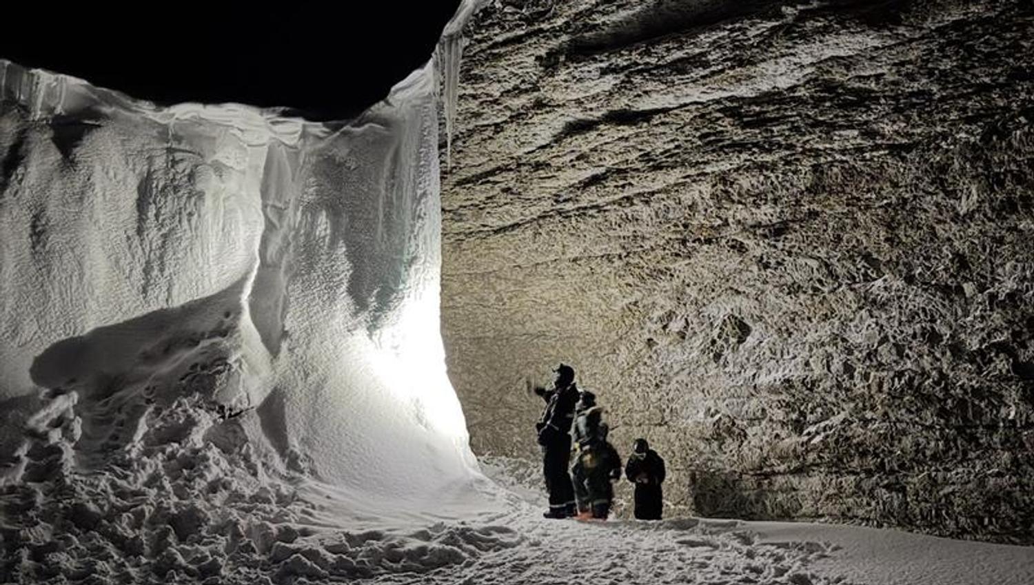 A group of people standing with headlamps, lighting up the frozen waterfall