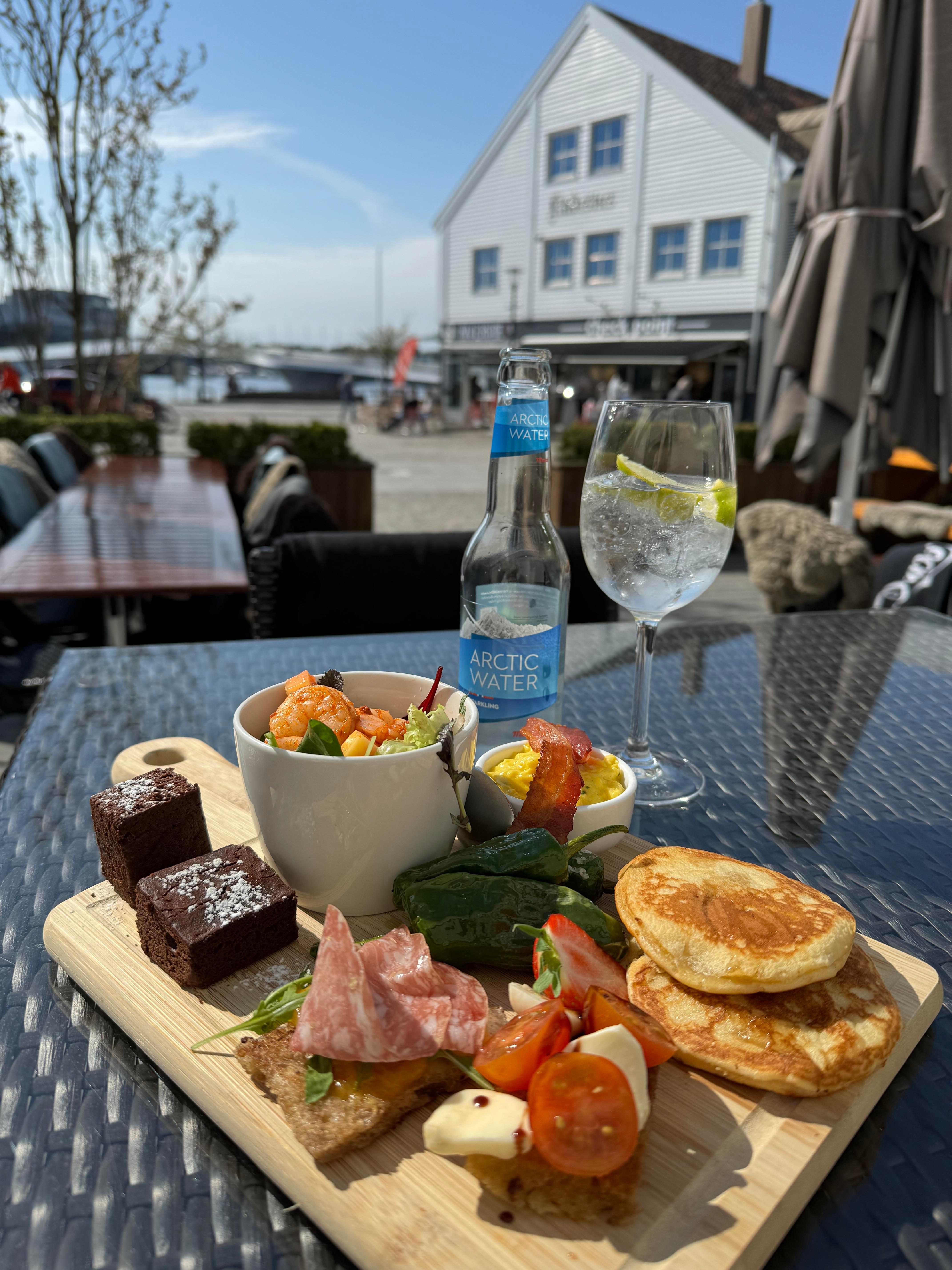 Matbilde tapastallerken, med kakestykke, liten skål med salat og scampi, stykke brød med salami, stykke brød med ost og tomater, snacks paprika, fiskekaker, bacon