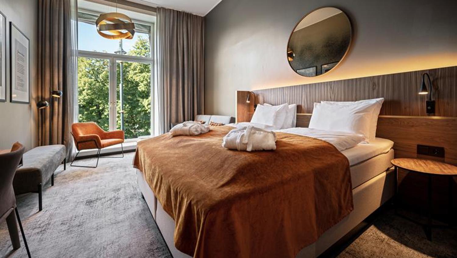 Room interior of deluxe room with a large double bed and a large window.