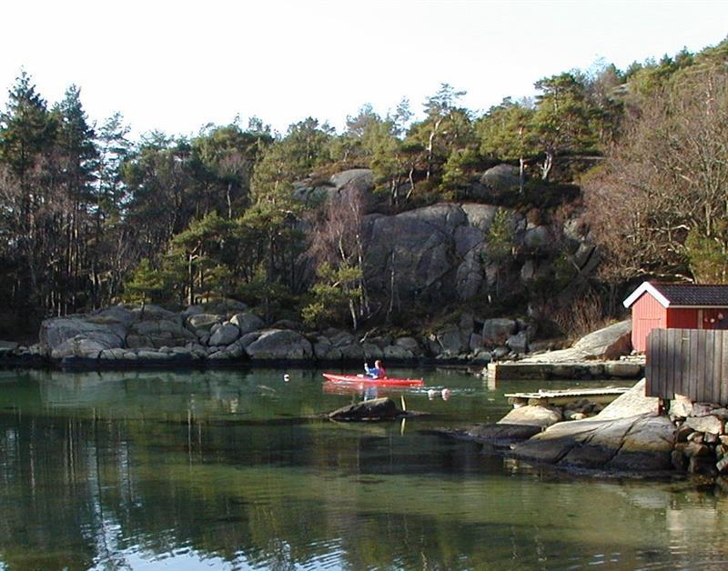 Bilde av en person i rød kajakk i vannet ved en brygge med en rød bygning