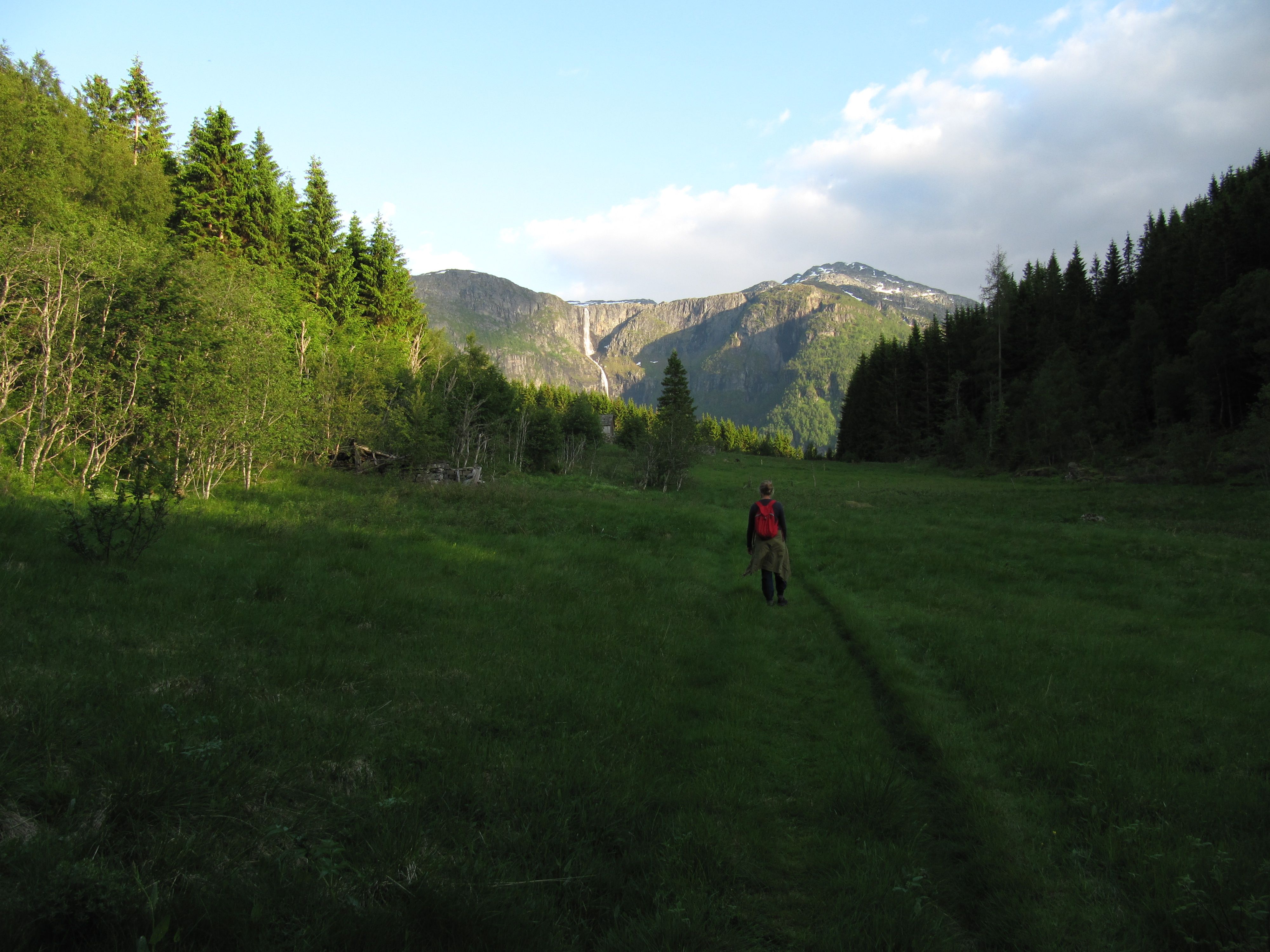Vandrar med raud sekk på stien gjennom dalen på Hovden rundt med fjell og fossar i horisonten.