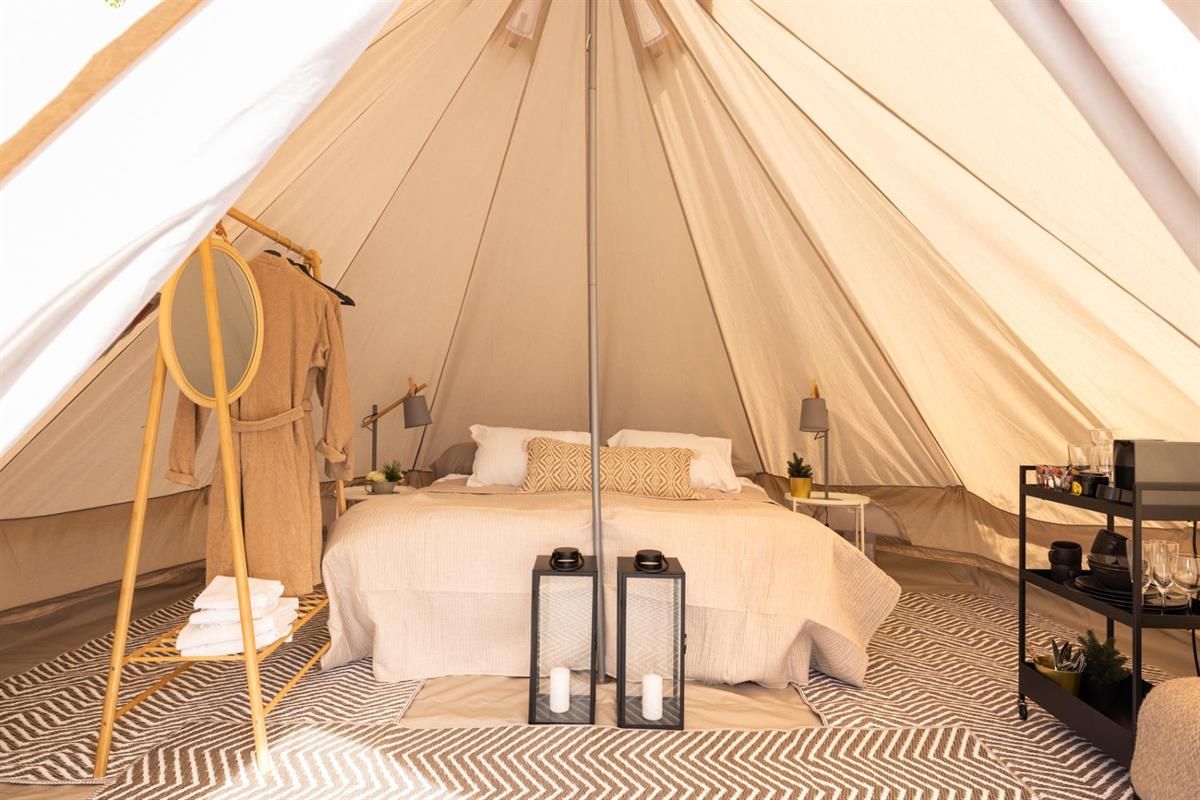 Innvendig bilde av et glampingtelt med seng, tepper og lanterne