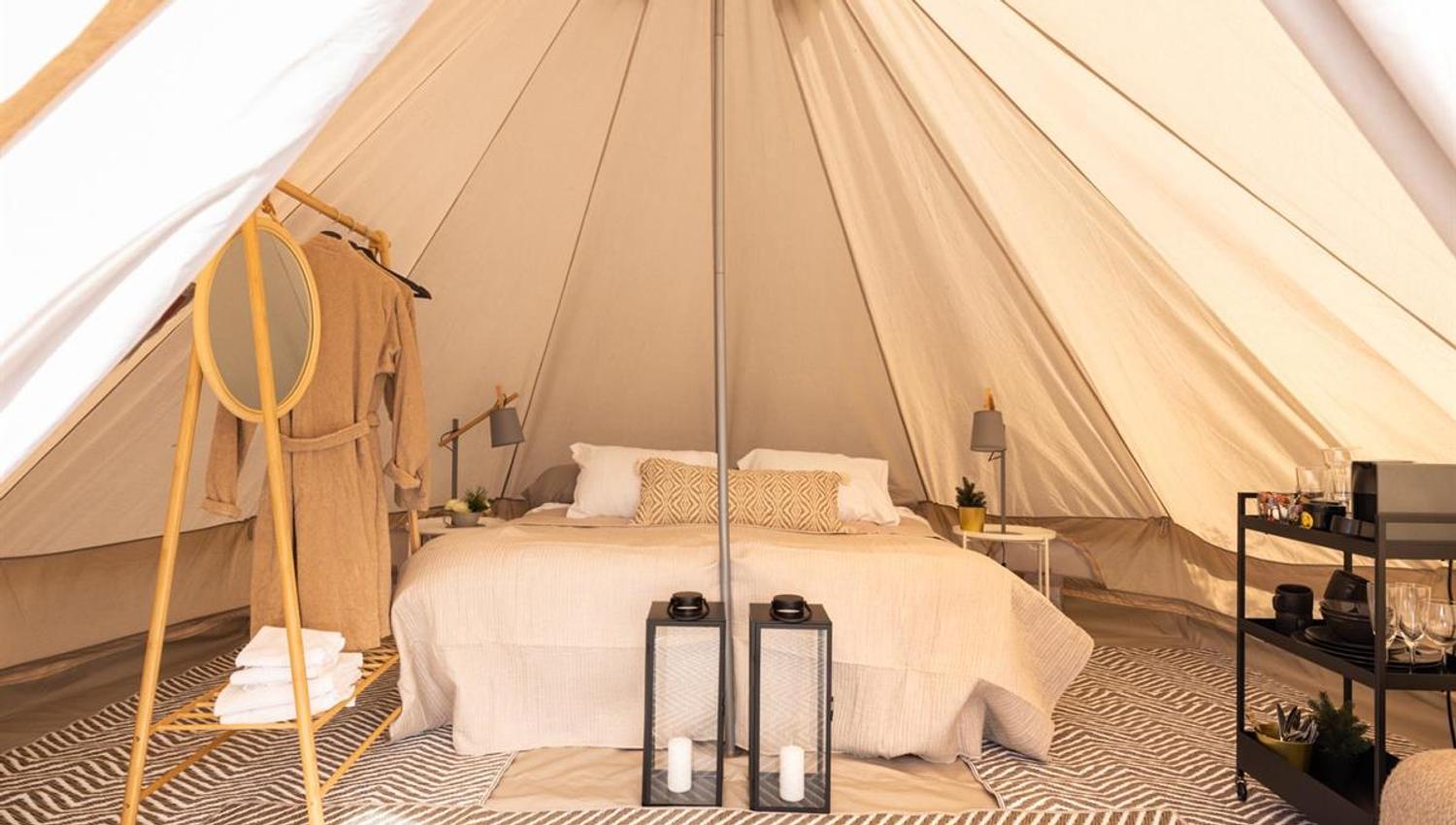 Innvendig bilde av et glampingtelt med seng, tepper og lanterne