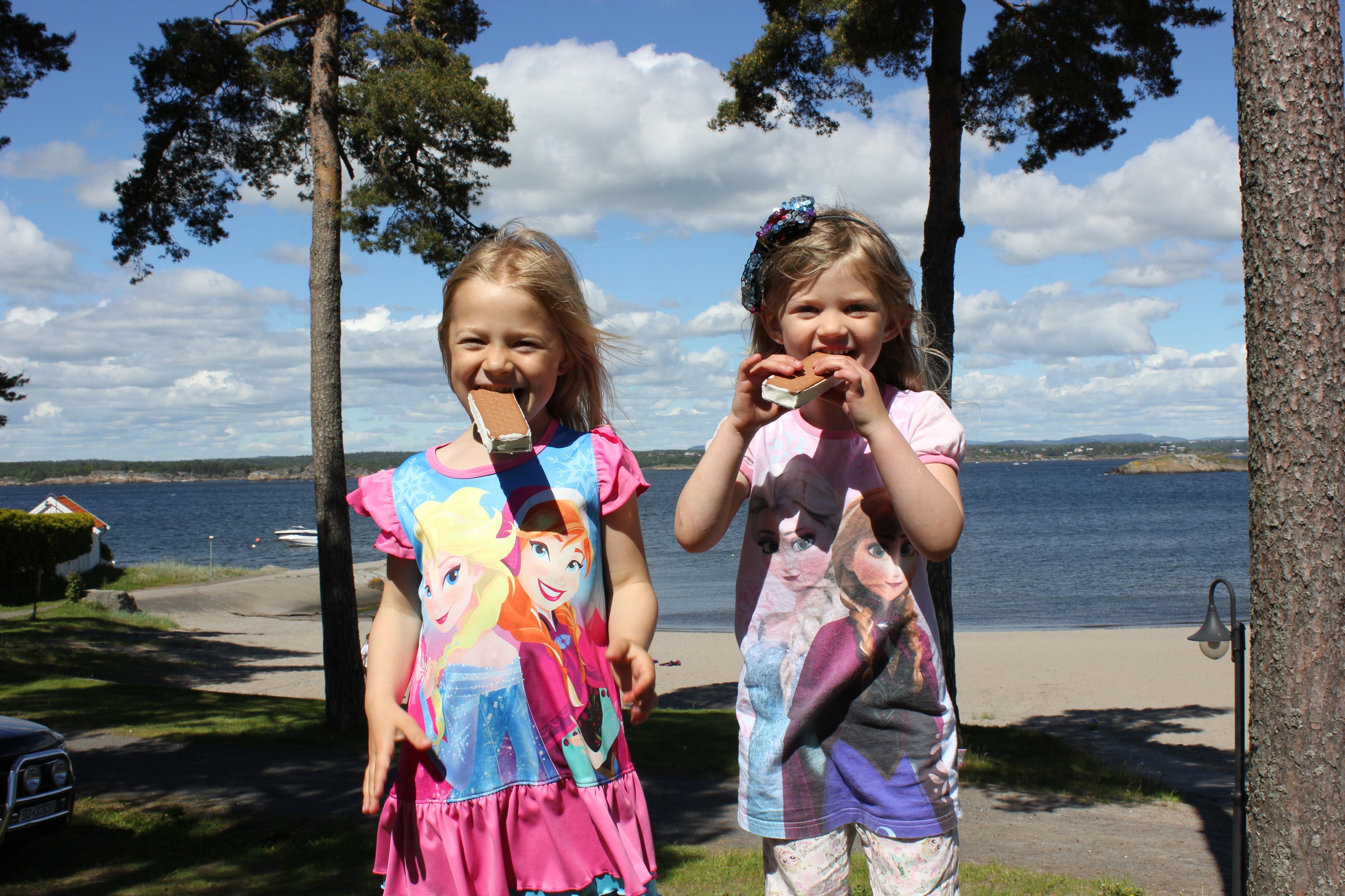 Two girls eat ice cream, beach and sea in the background