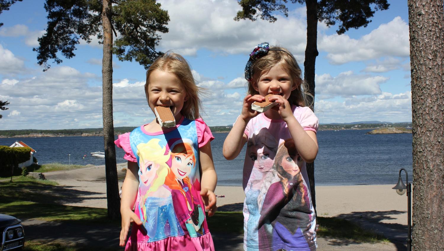 Two girls eat ice cream, beach and sea in the background