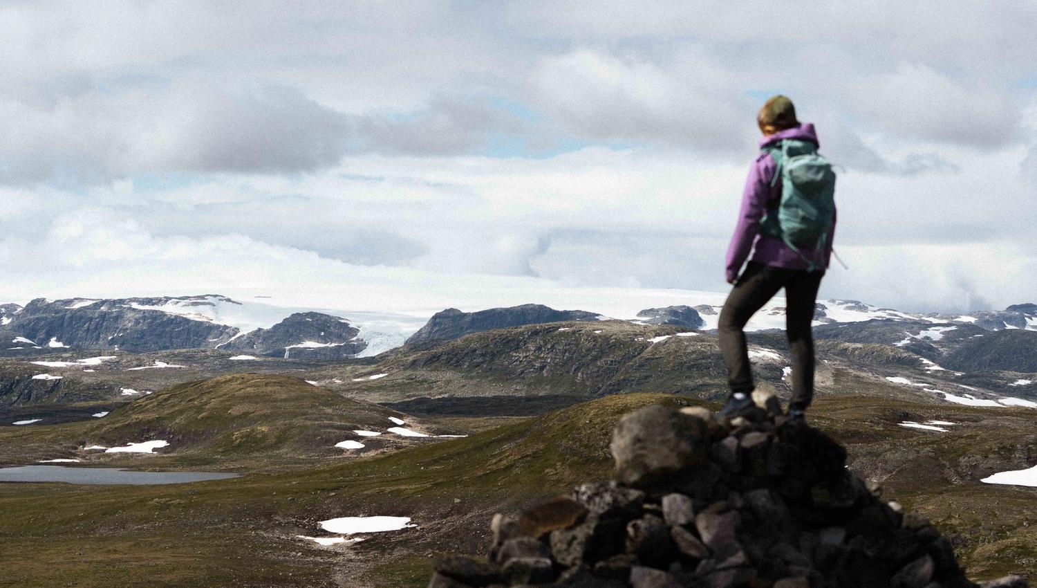 A woman standing on a mountain top gazing towards the Hardangerjøkulen glacier.