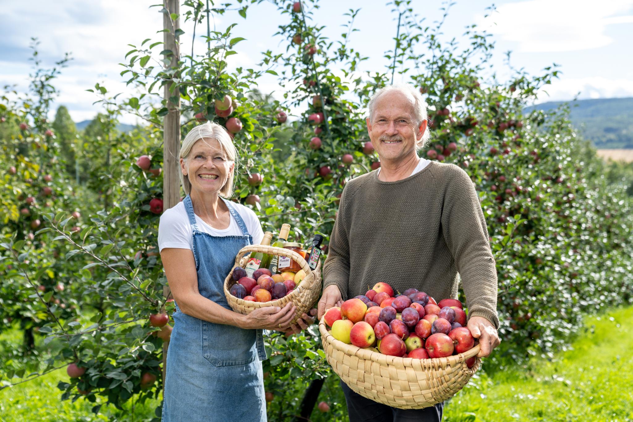 Elderly couple standing in front of fruit trees with fruit basket in hands 