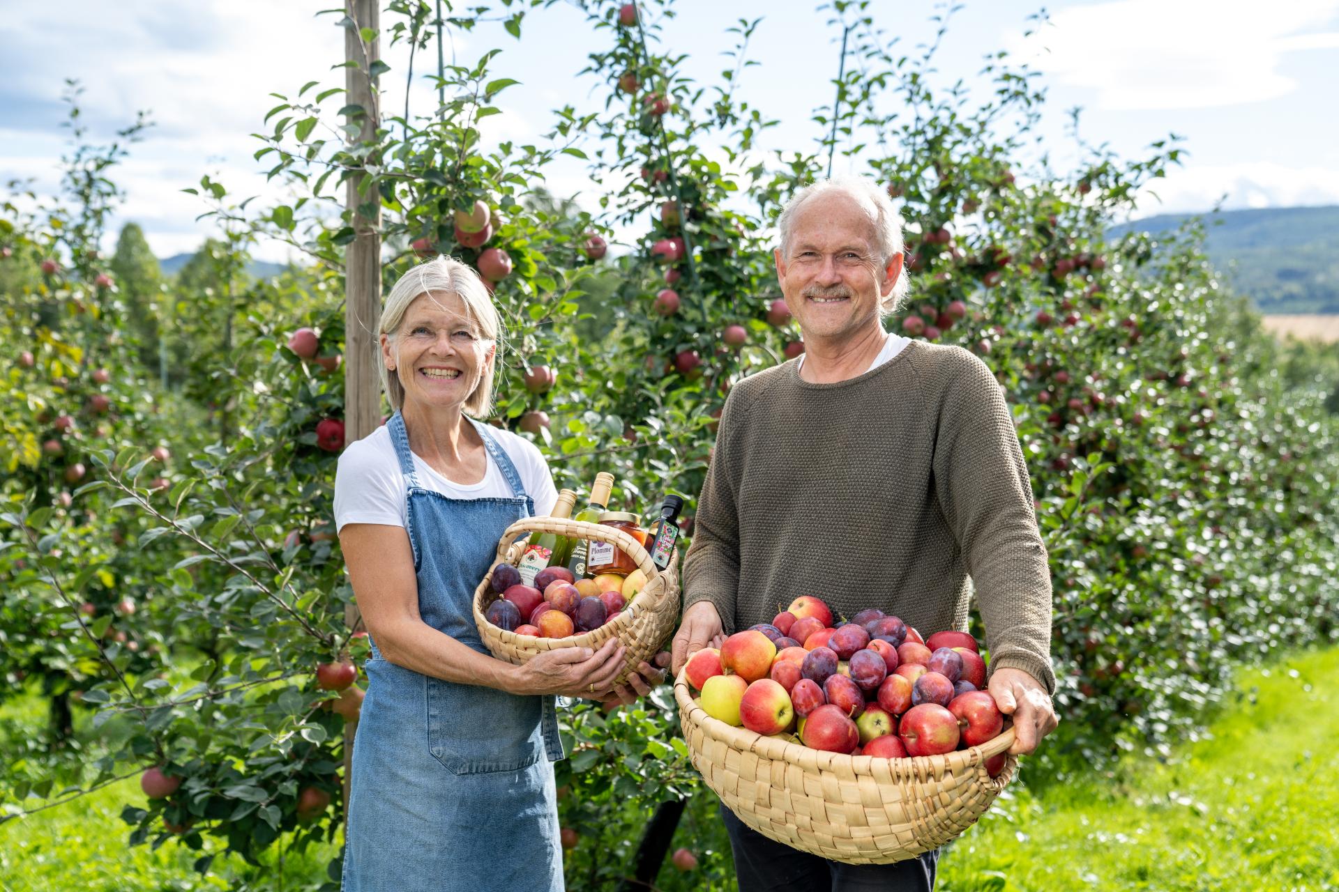 Elderly couple standing in front of fruit trees with fruit basket in hands