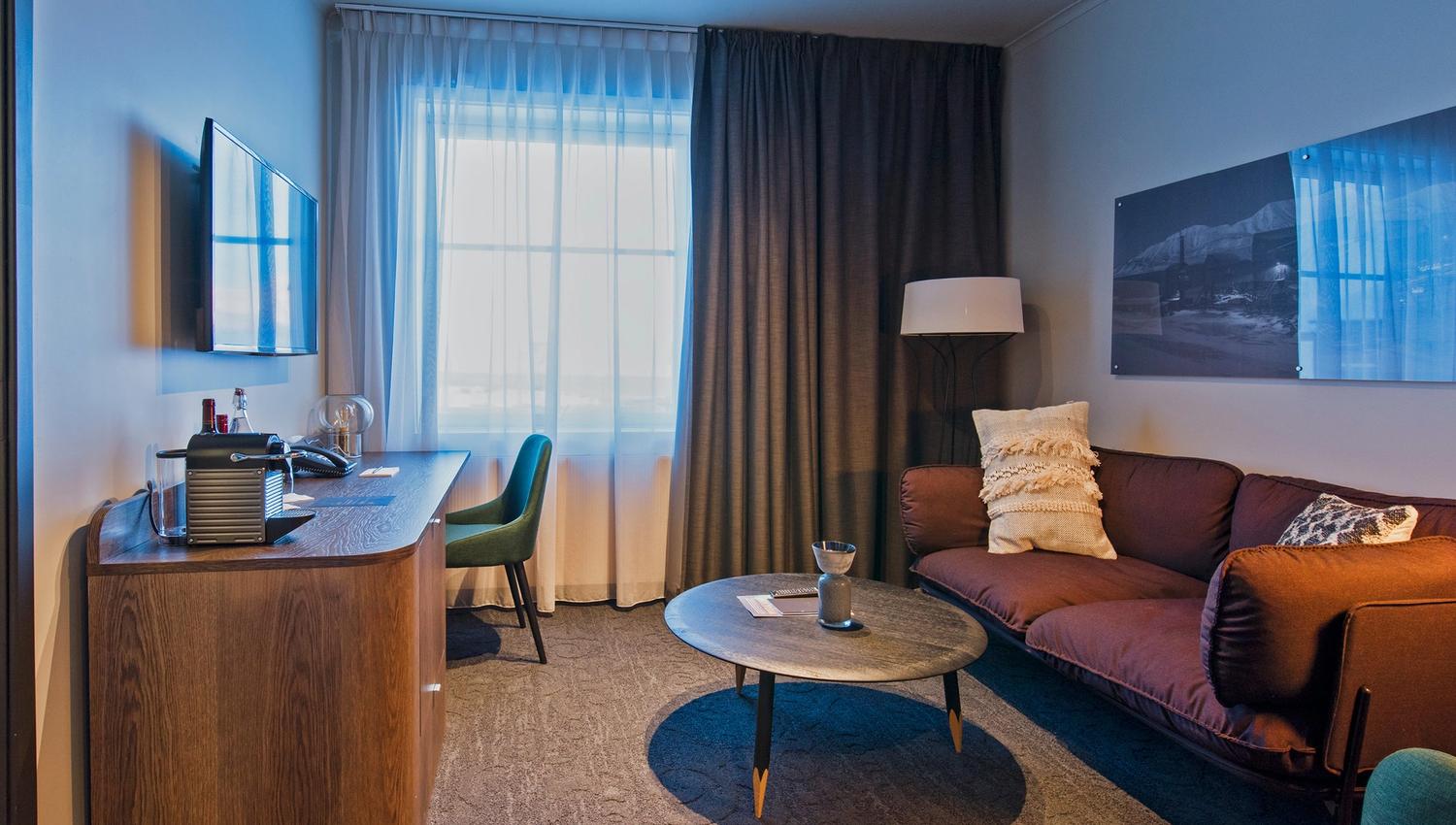 Et hotellrom med en sofa, kaffebord og arbeidspult