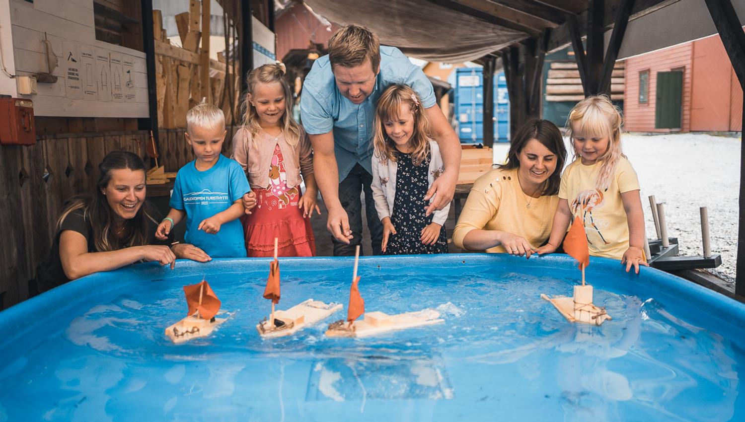 A family playing with small sailboats on water at Hardanger Maritime Center.