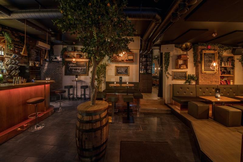 Bar interior with bar counter, bar stools, small tables and chairs, and a tree standing in a barrel in the middle of the room.