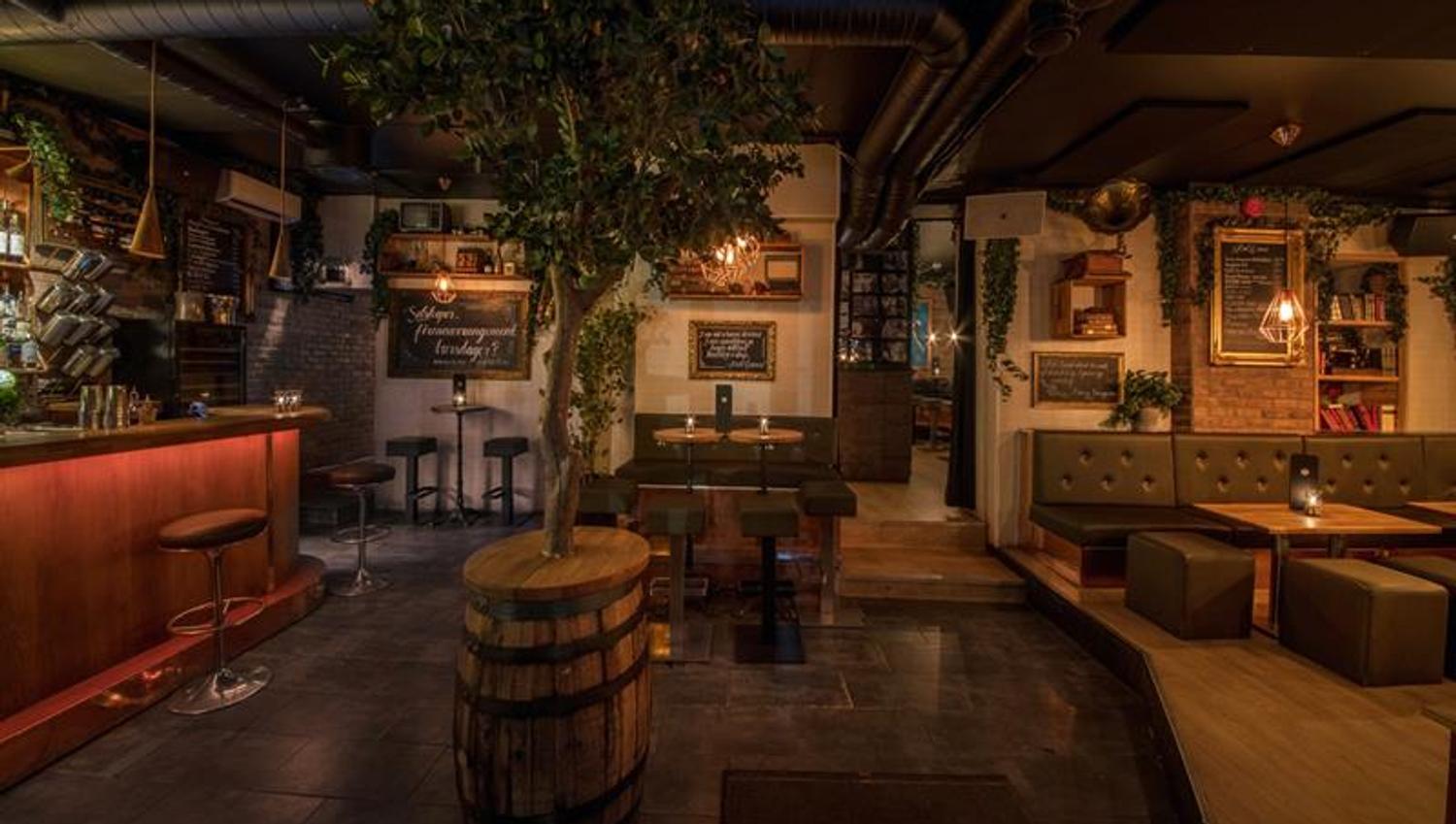 Bar interior with bar counter, bar stools, small tables and chairs, and a tree standing in a barrel in the middle of the room.