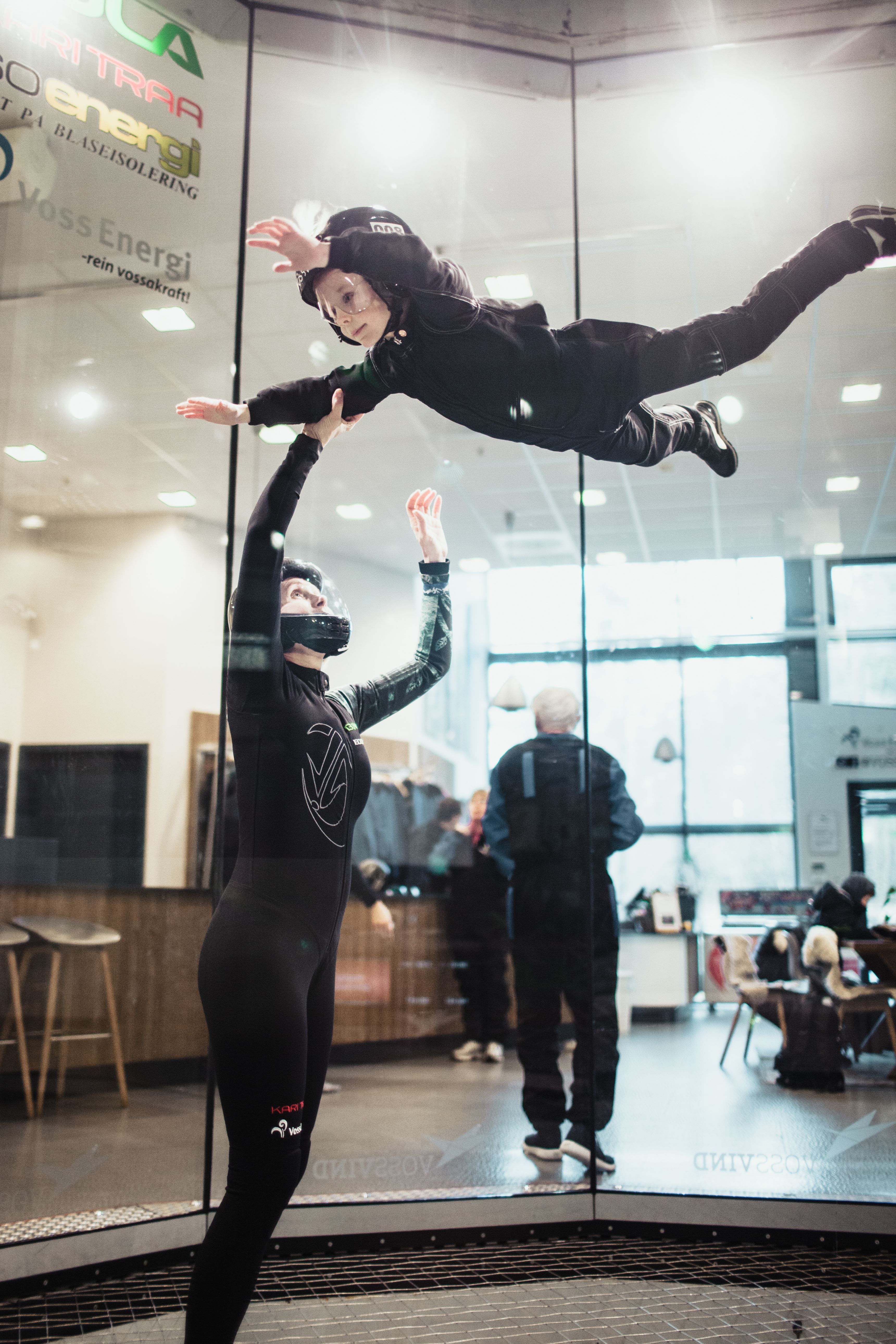 Child flying guided by an instructor inside the wind tunnel, arms and legs extended for stability.