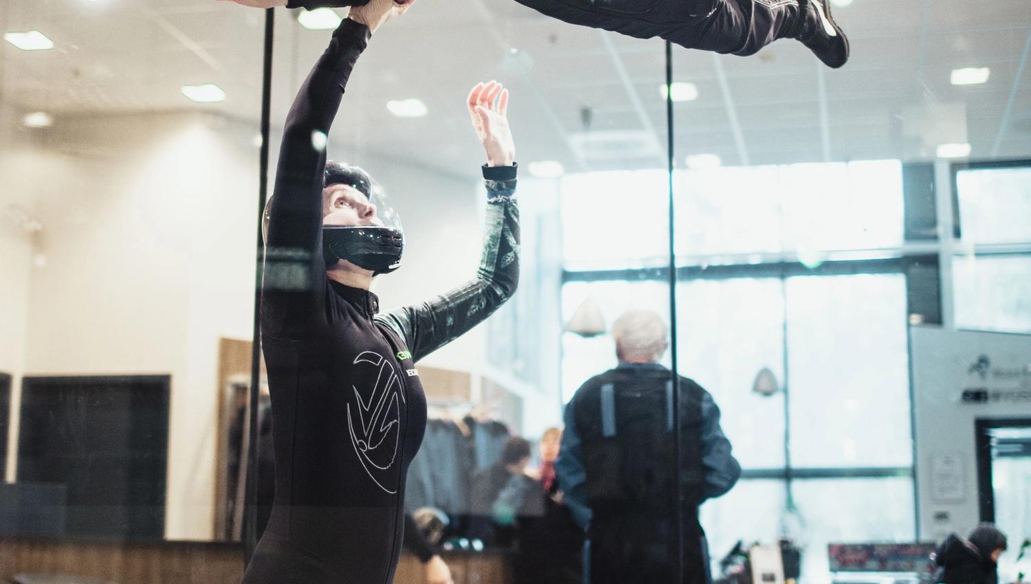 Child flying guided by an instructor inside the wind tunnel, arms and legs extended for stability.