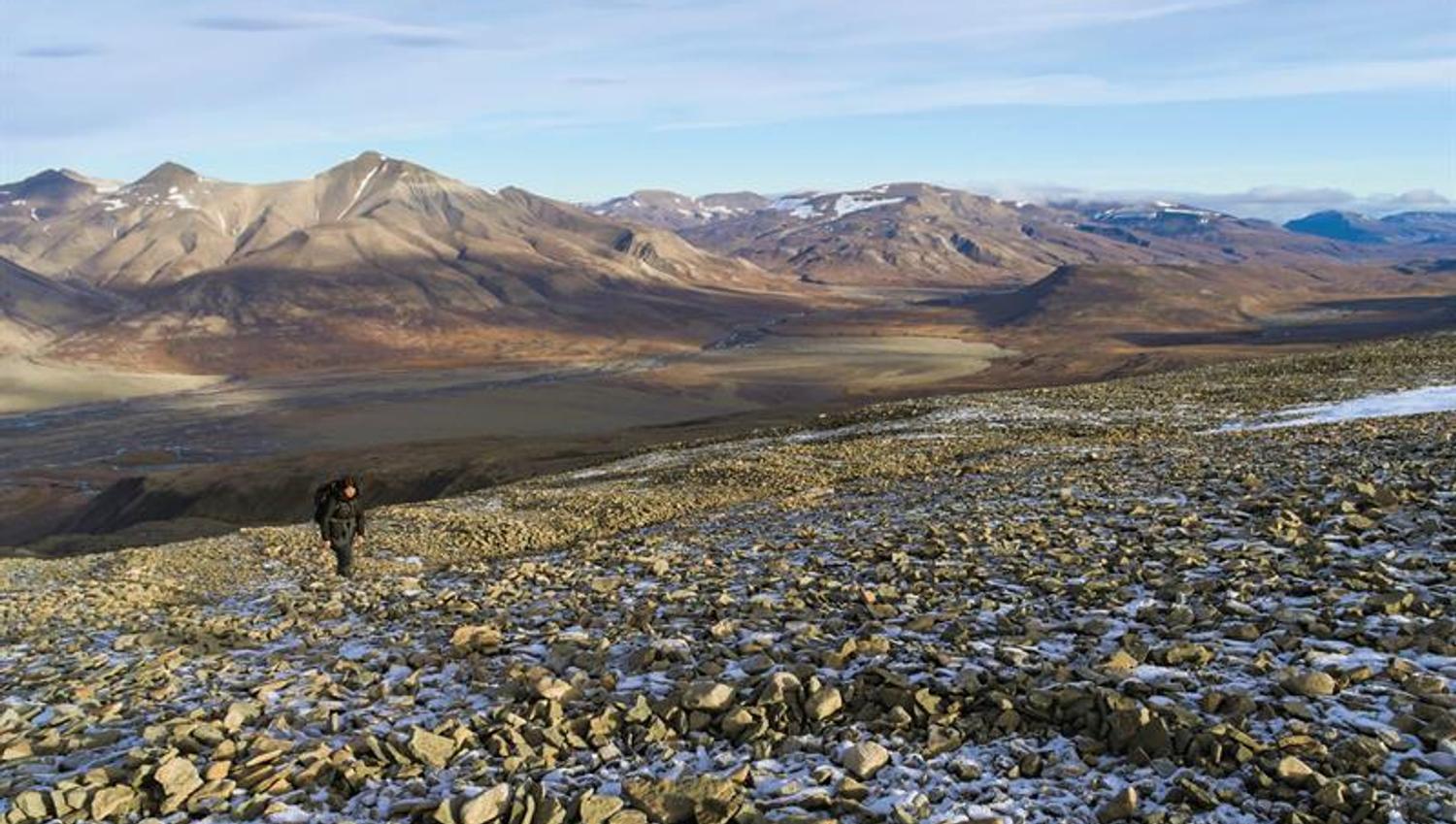 En person som går opp en steinete bakke med bakgrunn av mange fine fjell