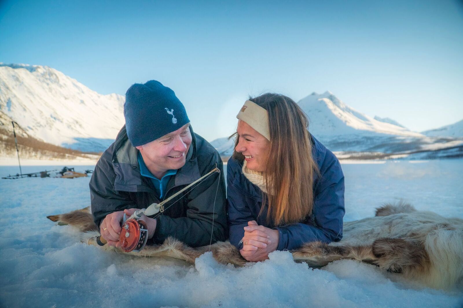 a couple laying on reindeer hides while ice fishing