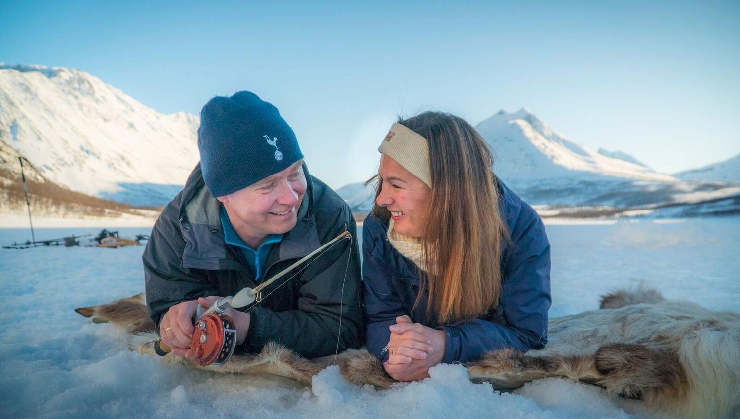 a couple laying on reindeer hides while ice fishing