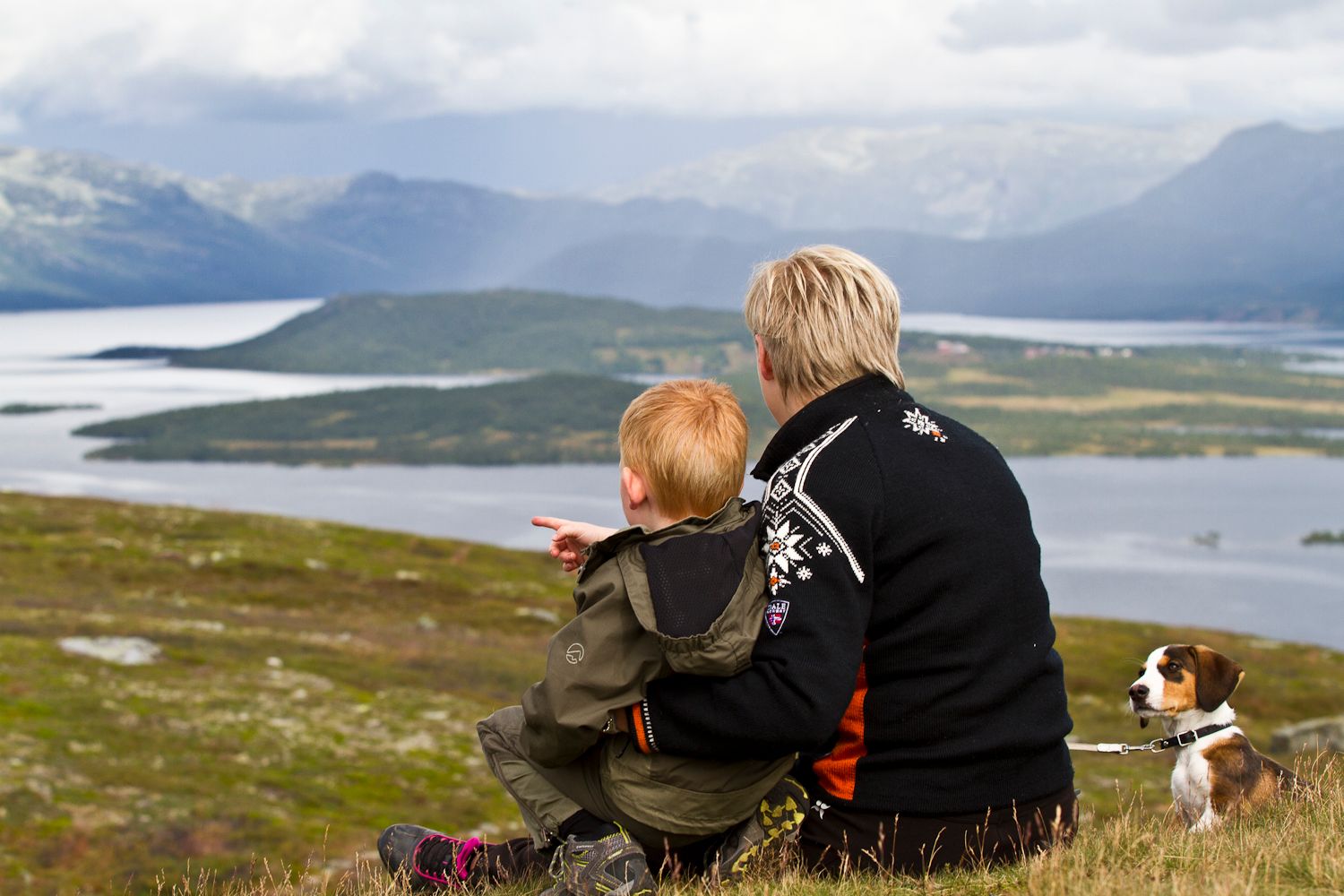 voksen og barn med hund sitter og ser ut over landskapet
