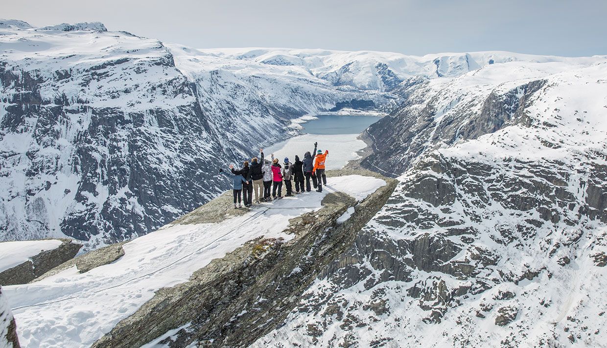 Group standing on the Trolltunga rock edge in winter, with panoramic mountain and fjord views.