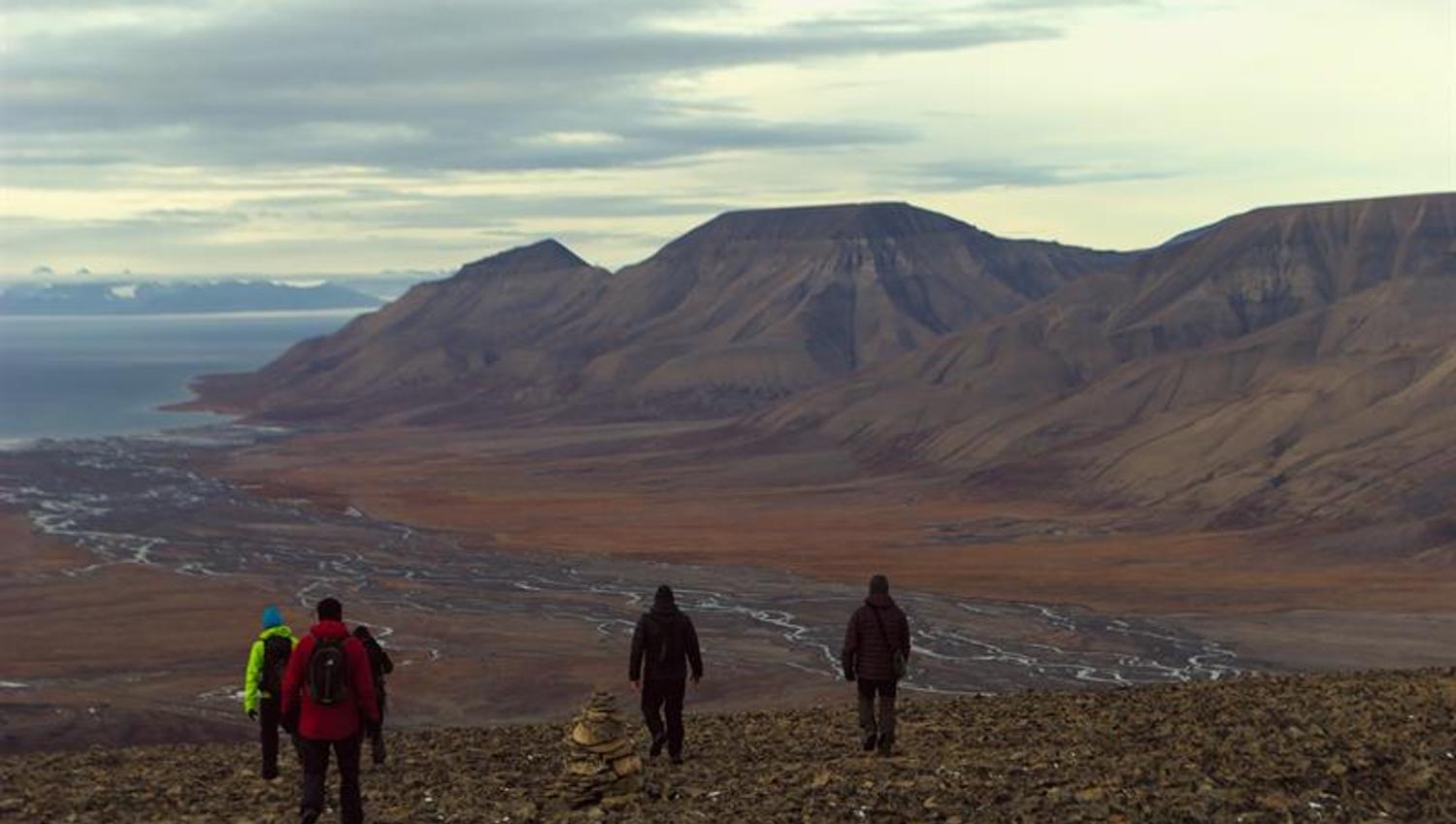 Personer som går ned fra et fjell med elver og fjell i bakgrunnen
