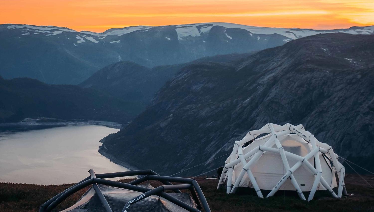 Geodetiske telt på fjelltoppen ved solnedgang med utsikt over en fjord.
