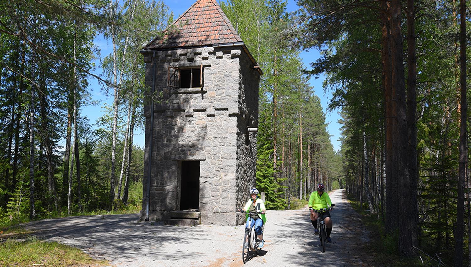2 syklister sykler forbi et tårn på sykkelveien "gamle Treungenbanen"