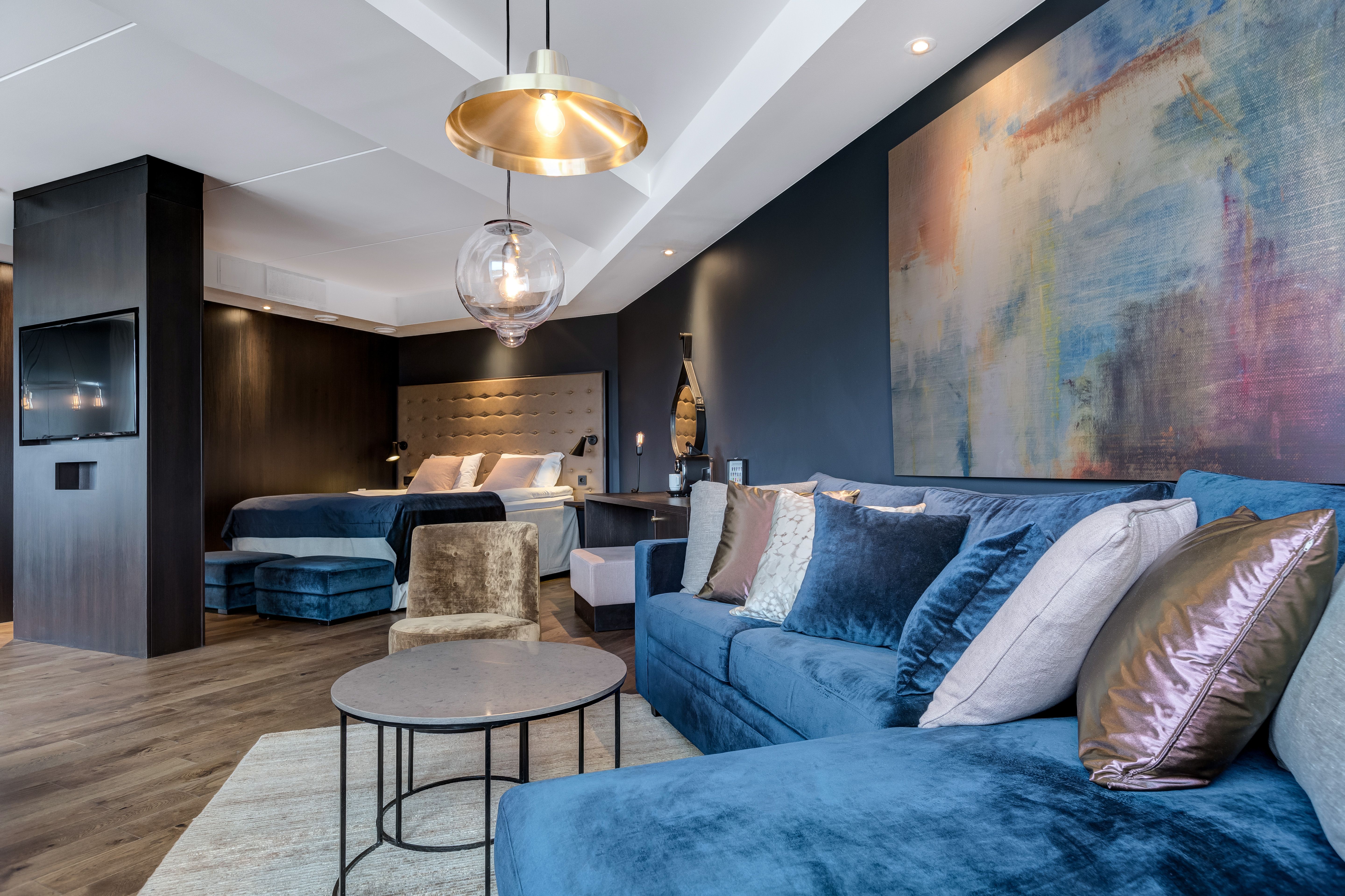 Et hotell rom med blå sofa , seng og bilde på vegg