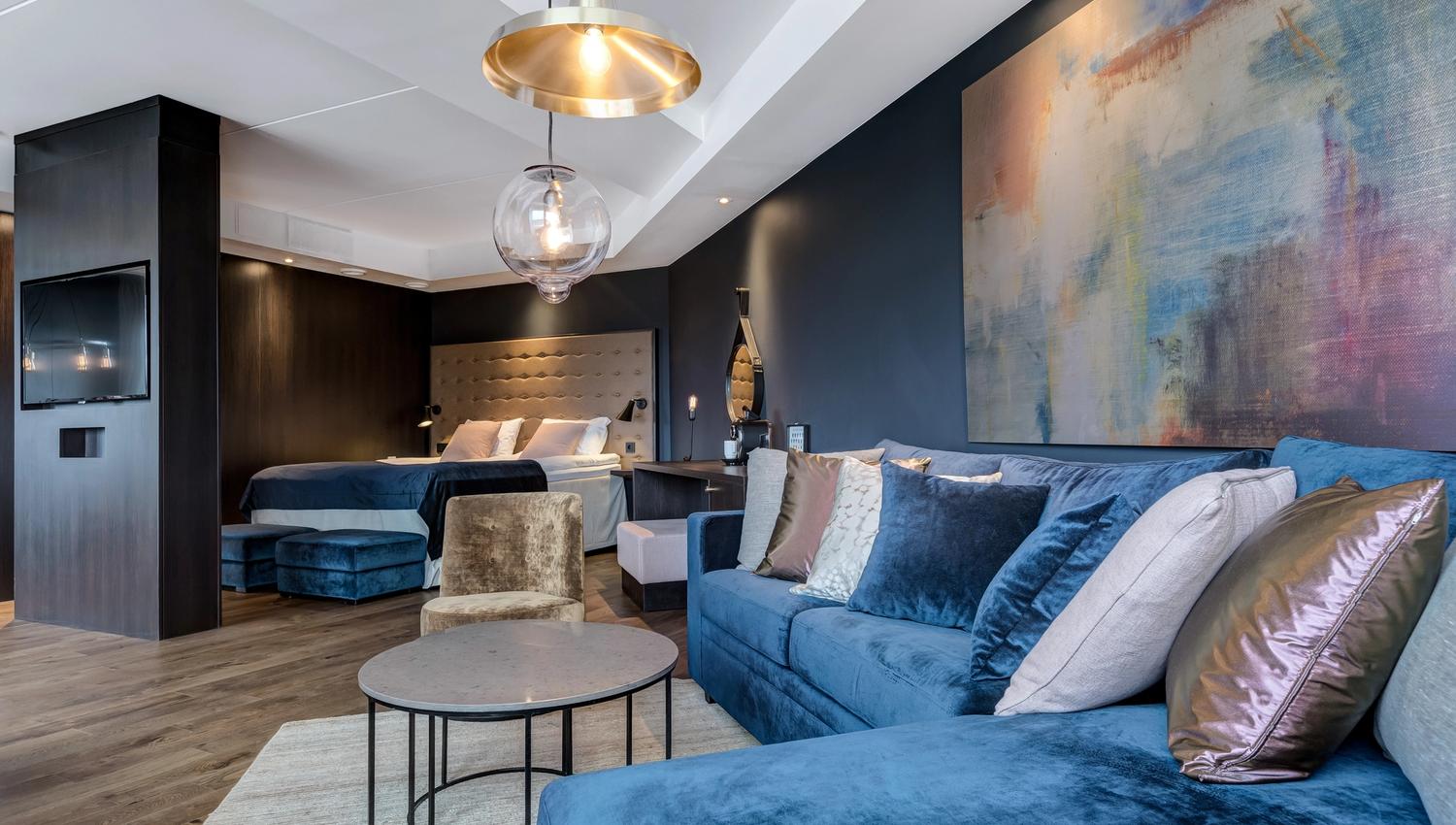 Et hotell rom med blå sofa , seng og bilde på vegg