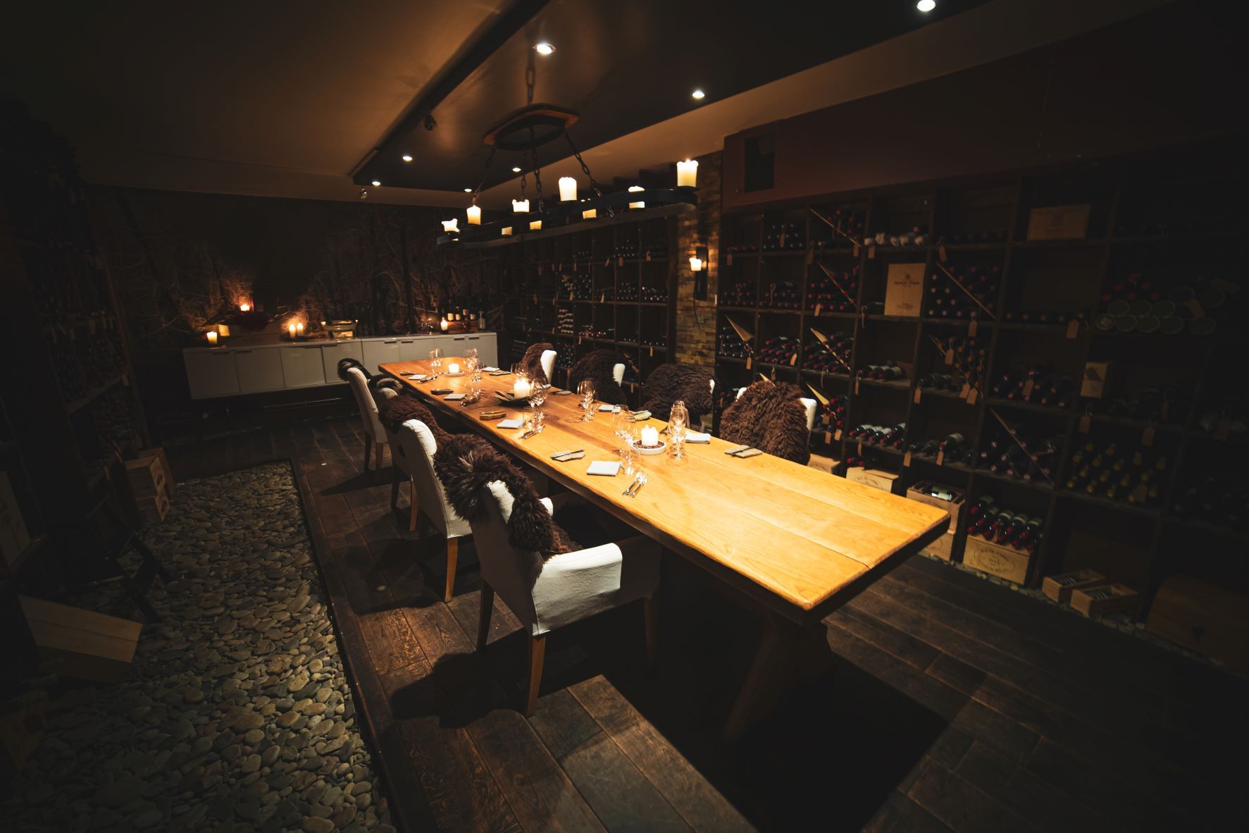 Et rom med et langbord og hyller fra gulv til tak med vinflasker langs rommets vegger