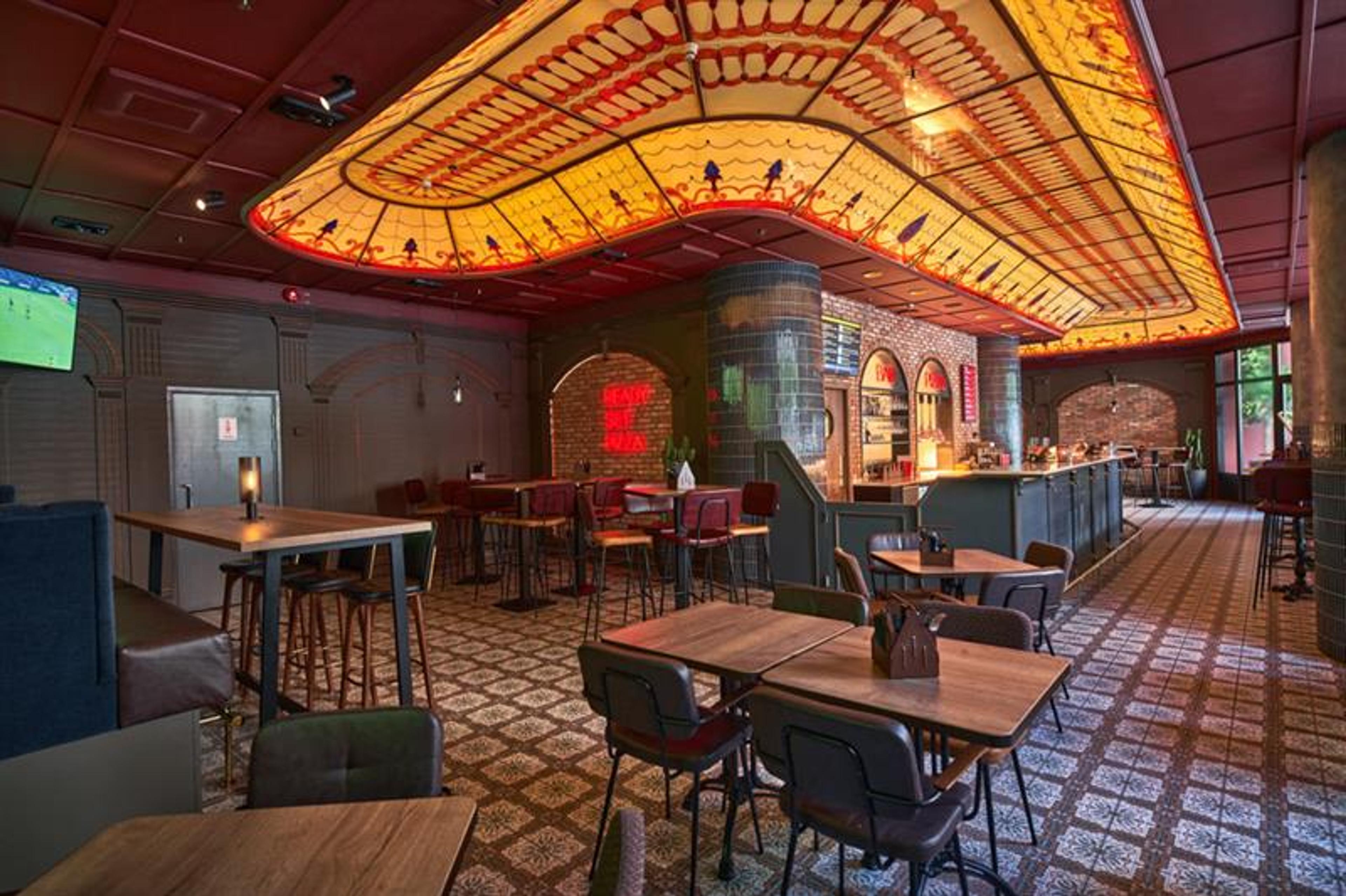 Restaurant interior with small square tables and chairs, bar and decorated glass ceiling above the bar