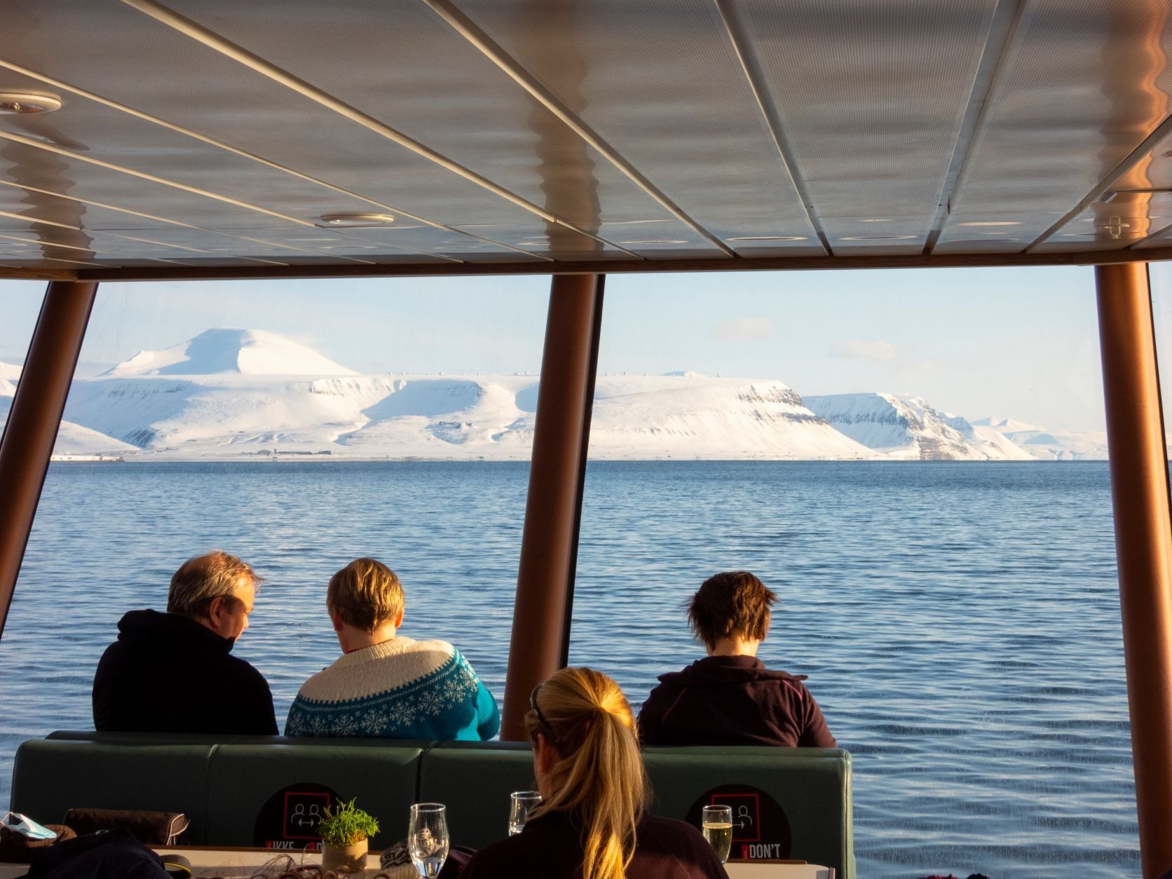 Guests sitting inside MS Bard with a fjord and mountains in the background