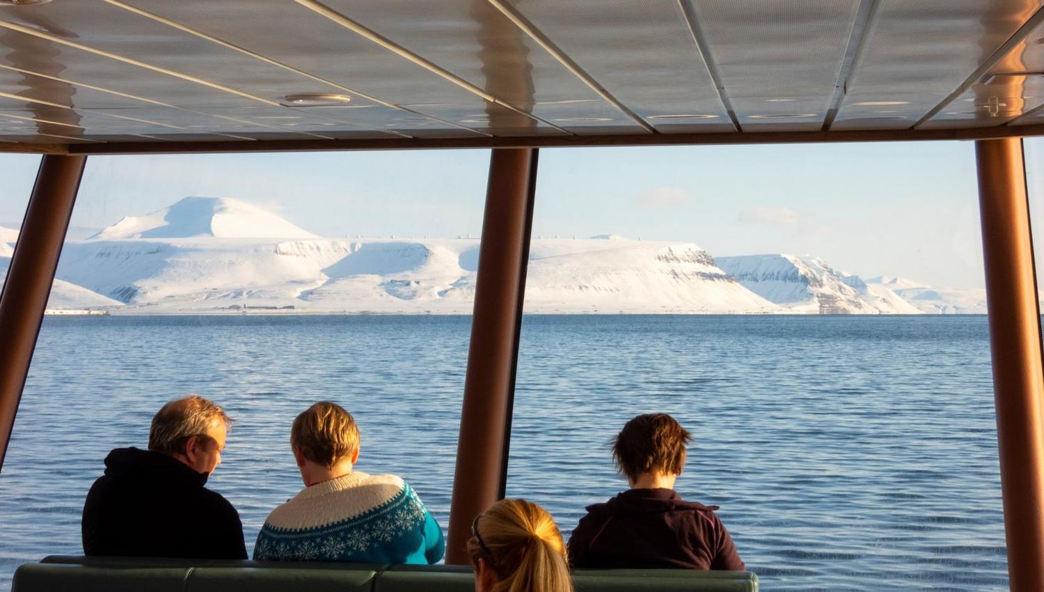 Guests sitting inside MS Bard with a fjord and mountains in the background