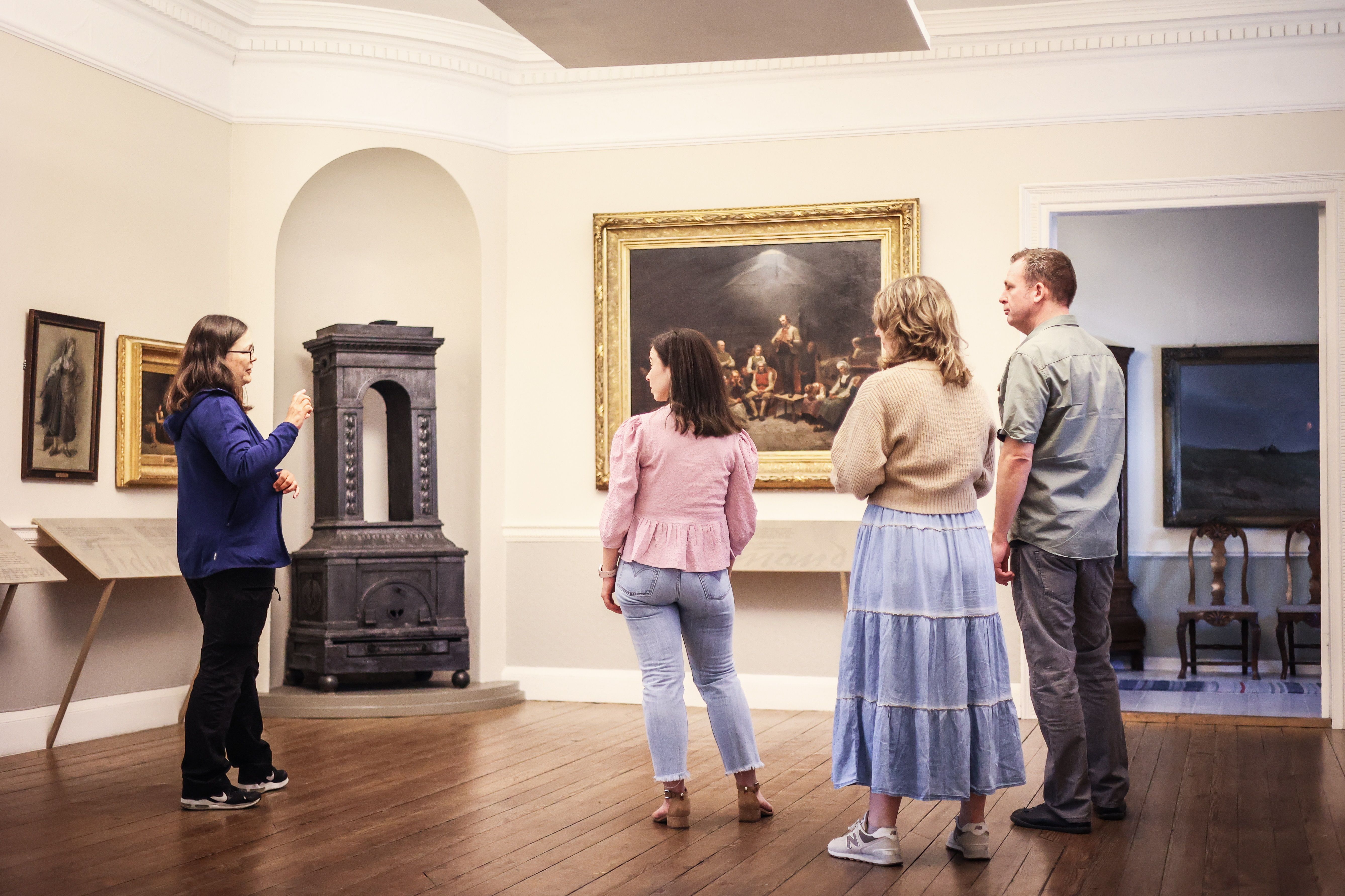 Fire personer inne på museet ser på det store maleriet «Haugianerne» på Mandal museum, der Adolph Tidemand skildrer lekpredikanten Hans Nielsen Hauges følgere.