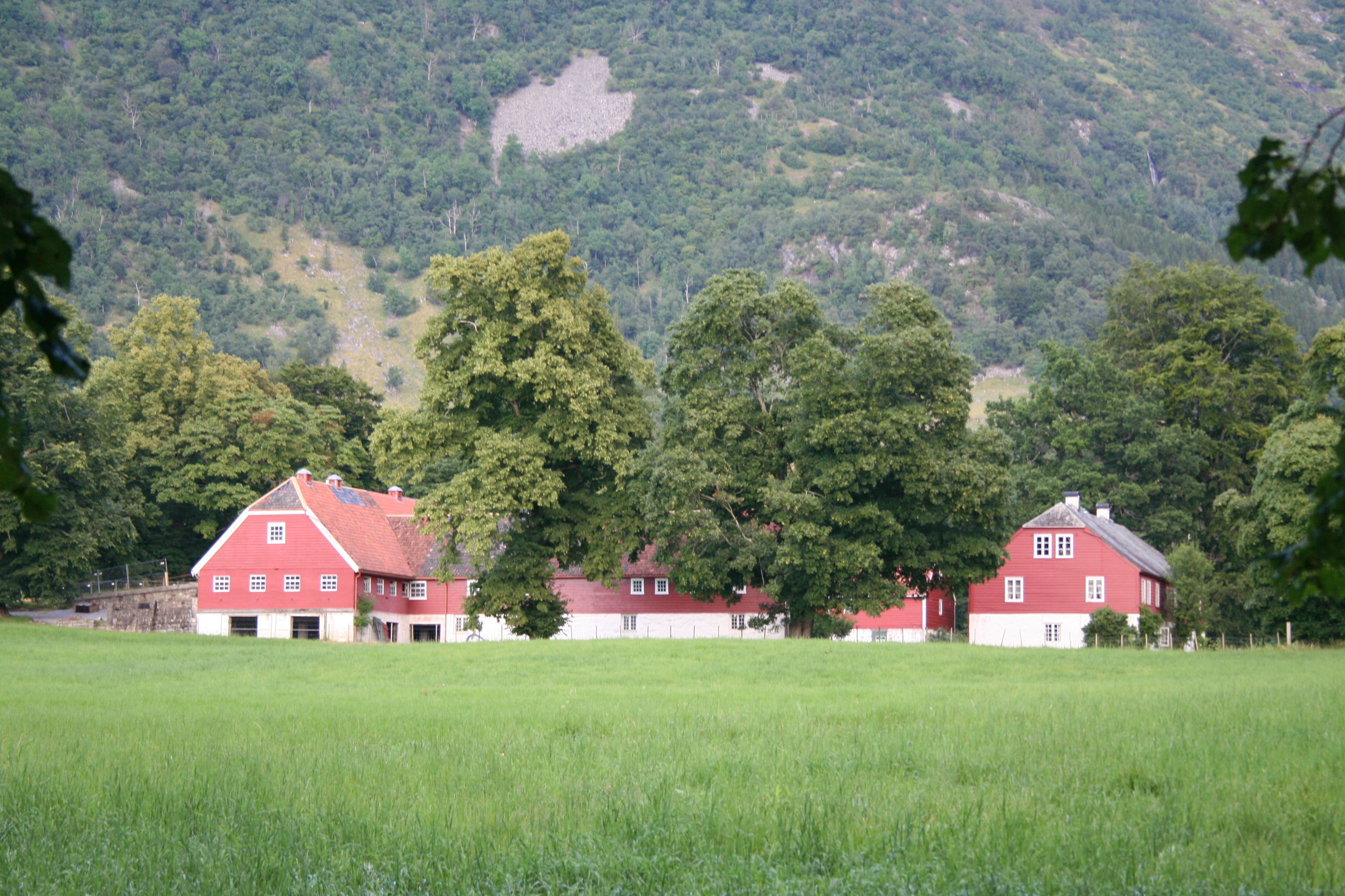 Dei raude uthusa ved Baroniet i Rosendal omgitt av grøne marker og majestetiske fjell.
